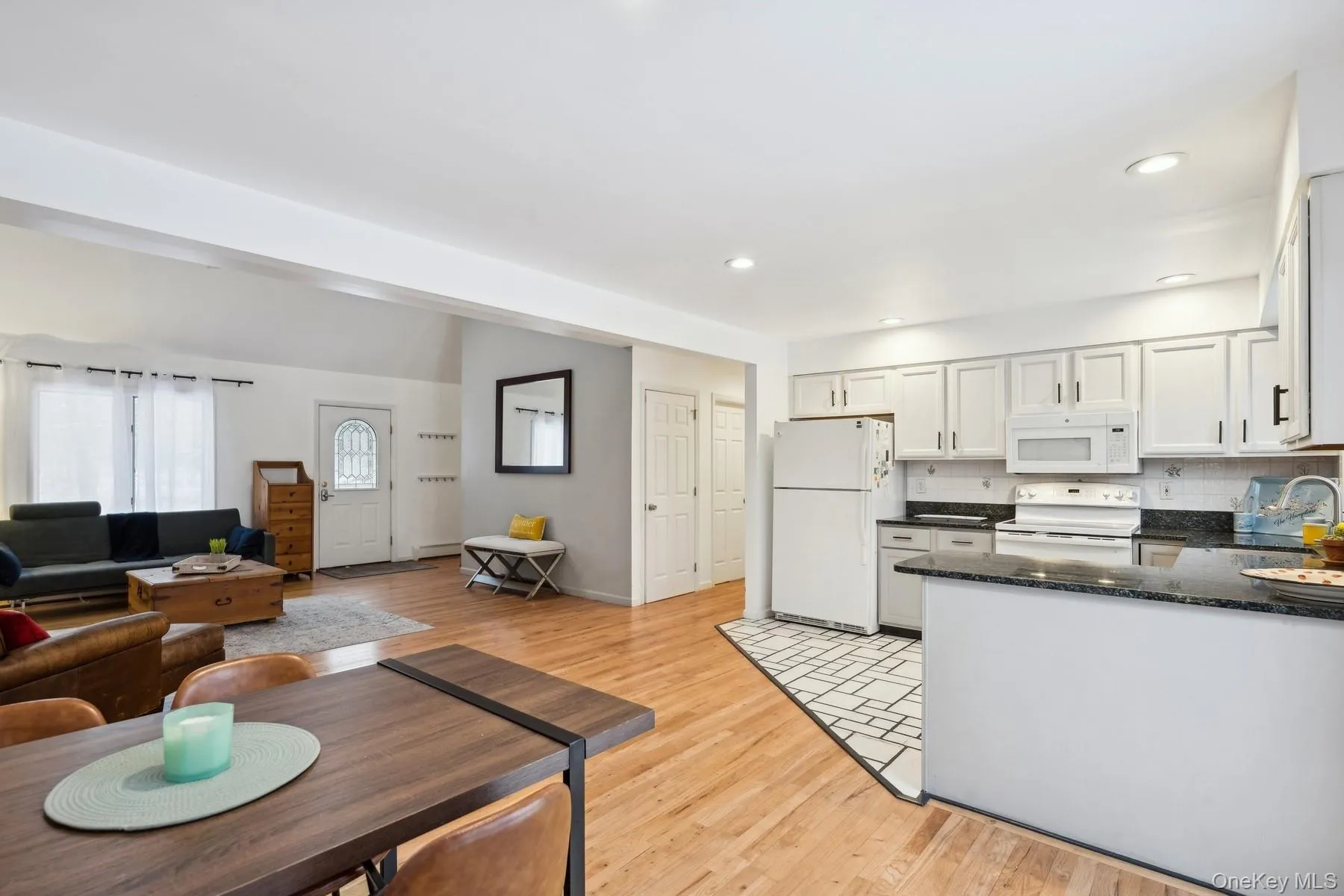 Kitchen with light wood-type flooring, tasteful backsplash, white appliances, sink, and white cabinets Kitchen with light wood-type flooring, tasteful backsplash, white appliances, sink, and white cabinets
