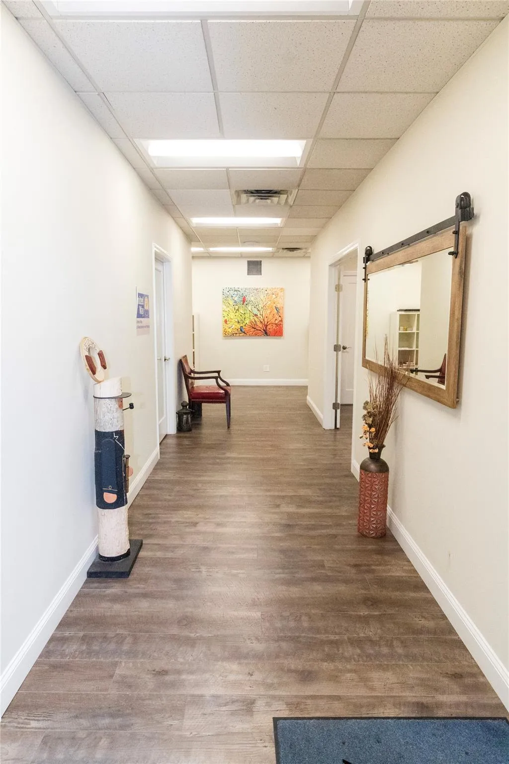 Hallway with a barn door, a drop ceiling, and wood-type flooring Hallway with a barn door, a drop ceiling, and wood-type flooring