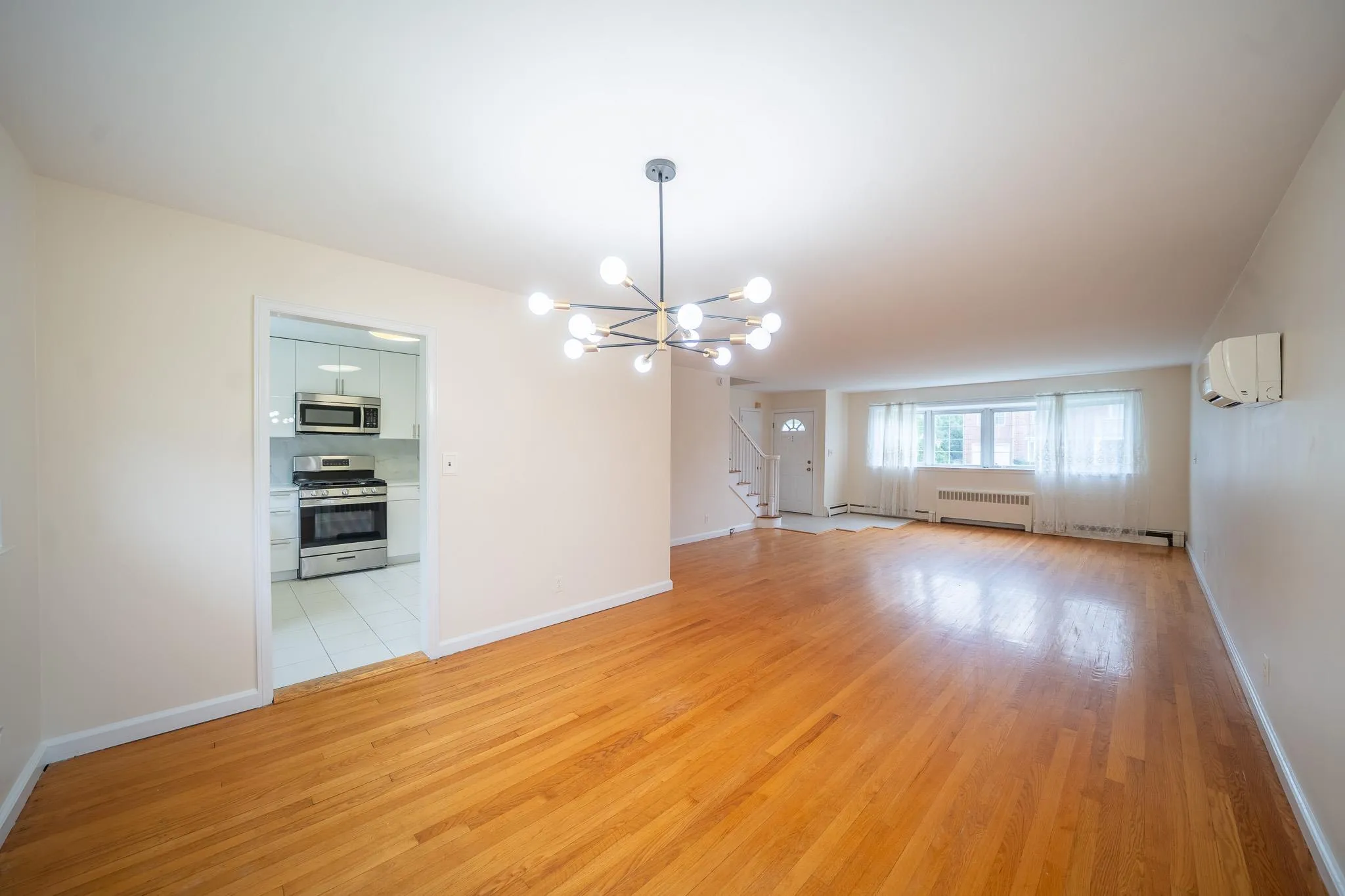 Unfurnished living room featuring radiator, a chandelier, a wall unit AC, and light wood-style floors Unfurnished living room featuring radiator, a chandelier, a wall unit AC, and light wood-style floors