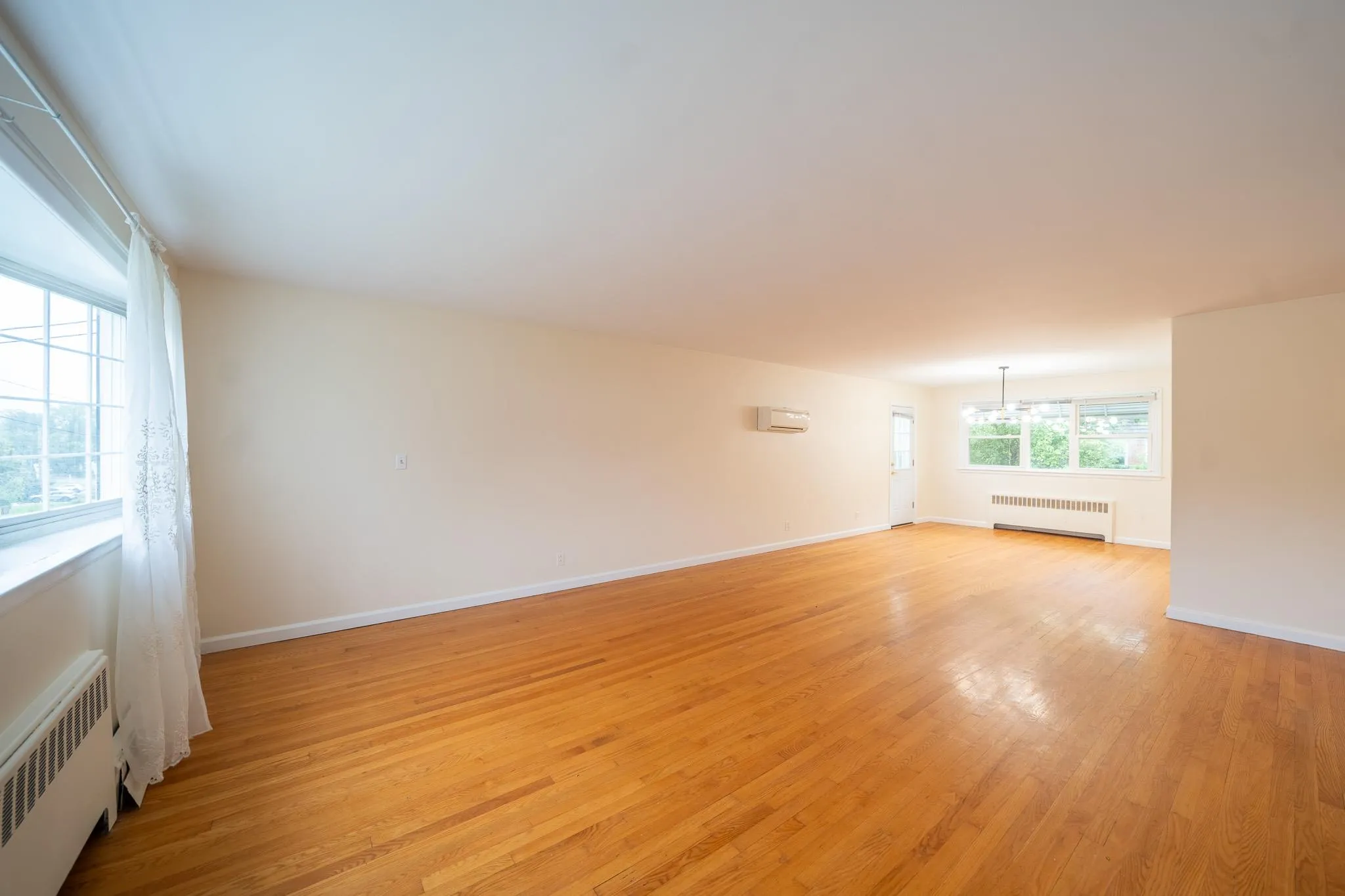 Spare room with radiator, light wood finished floors, a chandelier, and a wall mounted AC Spare room with radiator, light wood finished floors, a chandelier, and a wall mounted AC