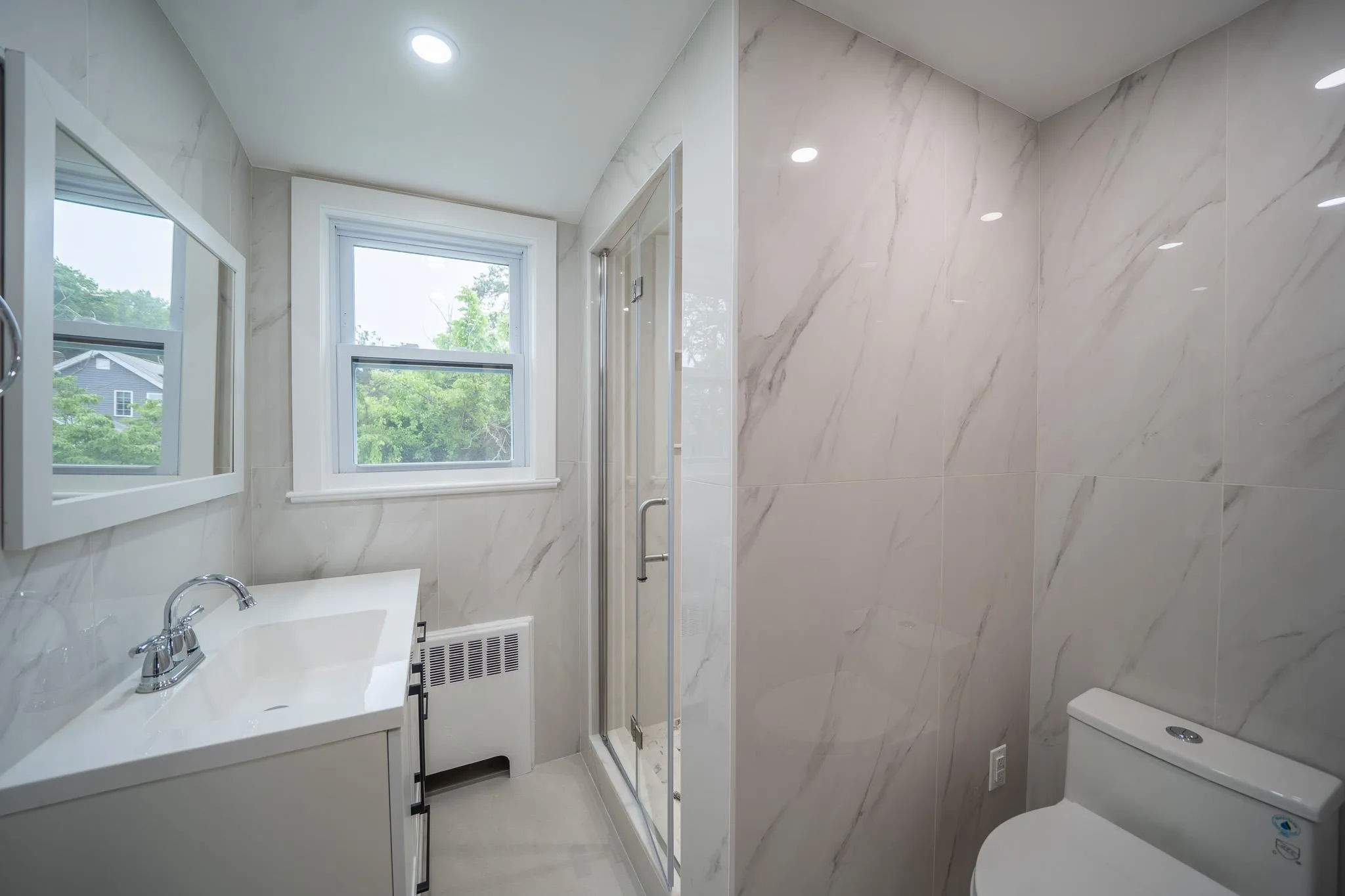 Bathroom with tile walls, vanity, a marble finish shower, and radiator Bathroom with tile walls, vanity, a marble finish shower, and radiator
