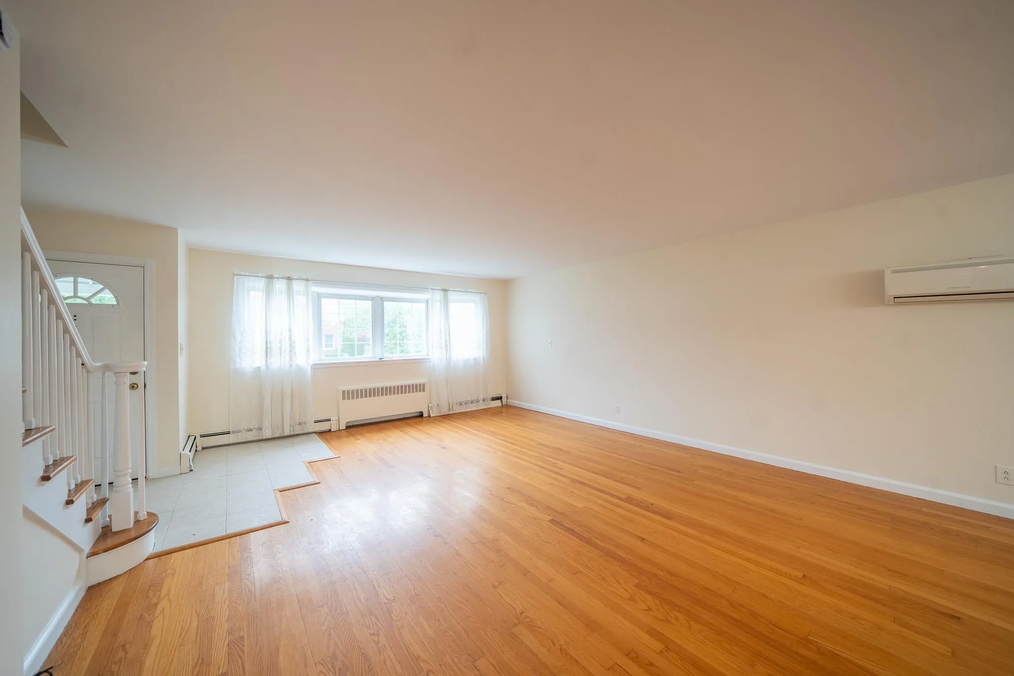 Unfurnished living room featuring an AC wall unit, radiator heating unit, light wood-style flooring, and healthy amount of natural light Unfurnished living room featuring an AC wall unit, radiator heating unit, light wood-style flooring, and healthy amount of natural light