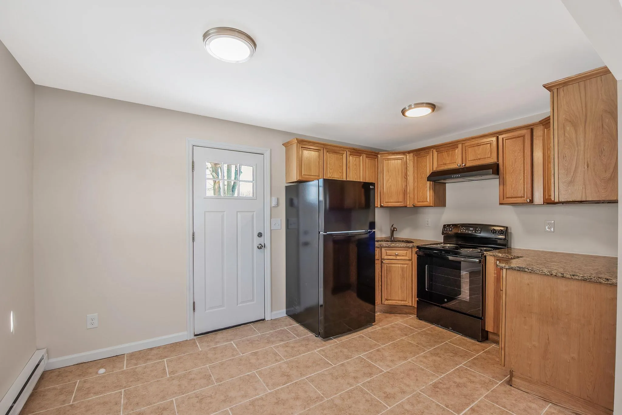 Kitchen featuring light stone counters, baseboard heating, sink, black appliances, and light tile patterned floors Kitchen featuring light stone counters, baseboard heating, sink, black appliances, and light tile patterned floors