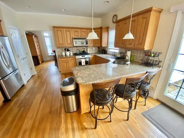 Kitchen with hanging light fixtures, stainless steel appliances, backsplash, kitchen peninsula, and a breakfast bar area Kitchen with hanging light fixtures, stainless steel appliances, backsplash, kitchen peninsula, and a breakfast bar area