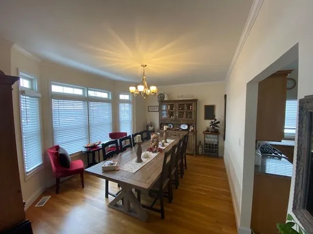 Dining space with hardwood / wood-style floors, crown molding, and an inviting chandelier Dining space with hardwood / wood-style floors, crown molding, and an inviting chandelier
