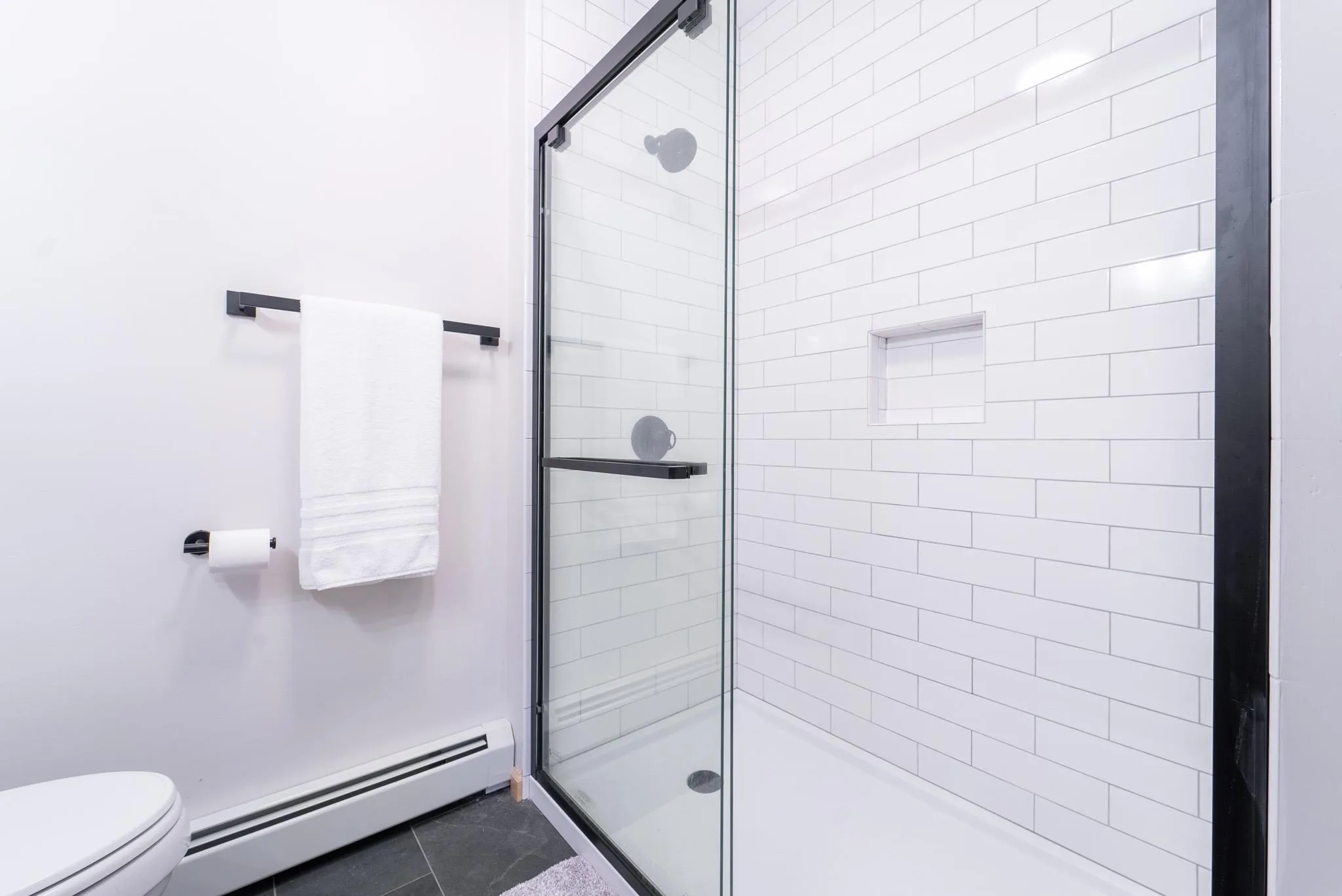 Bathroom featuring toilet, tile patterned floors, walk in shower, and a baseboard heating unit Bathroom featuring toilet, tile patterned floors, walk in shower, and a baseboard heating unit