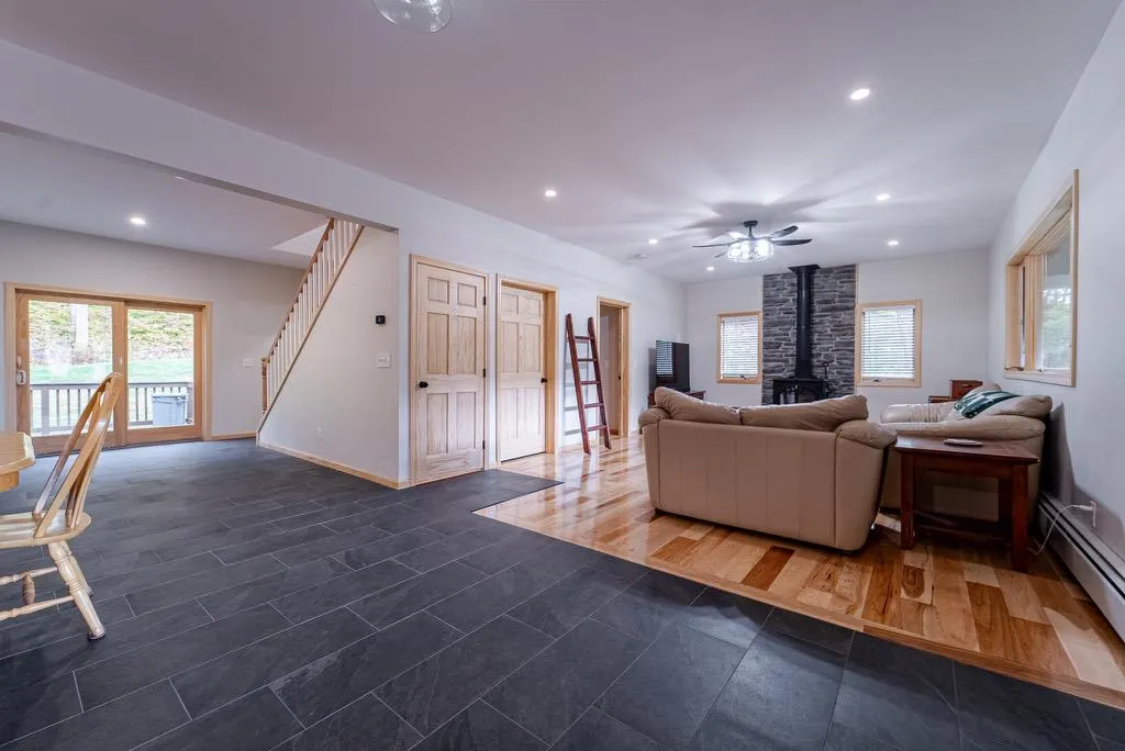 Living room featuring baseboard heating, a wood stove, and ceiling fan Living room featuring baseboard heating, a wood stove, and ceiling fan