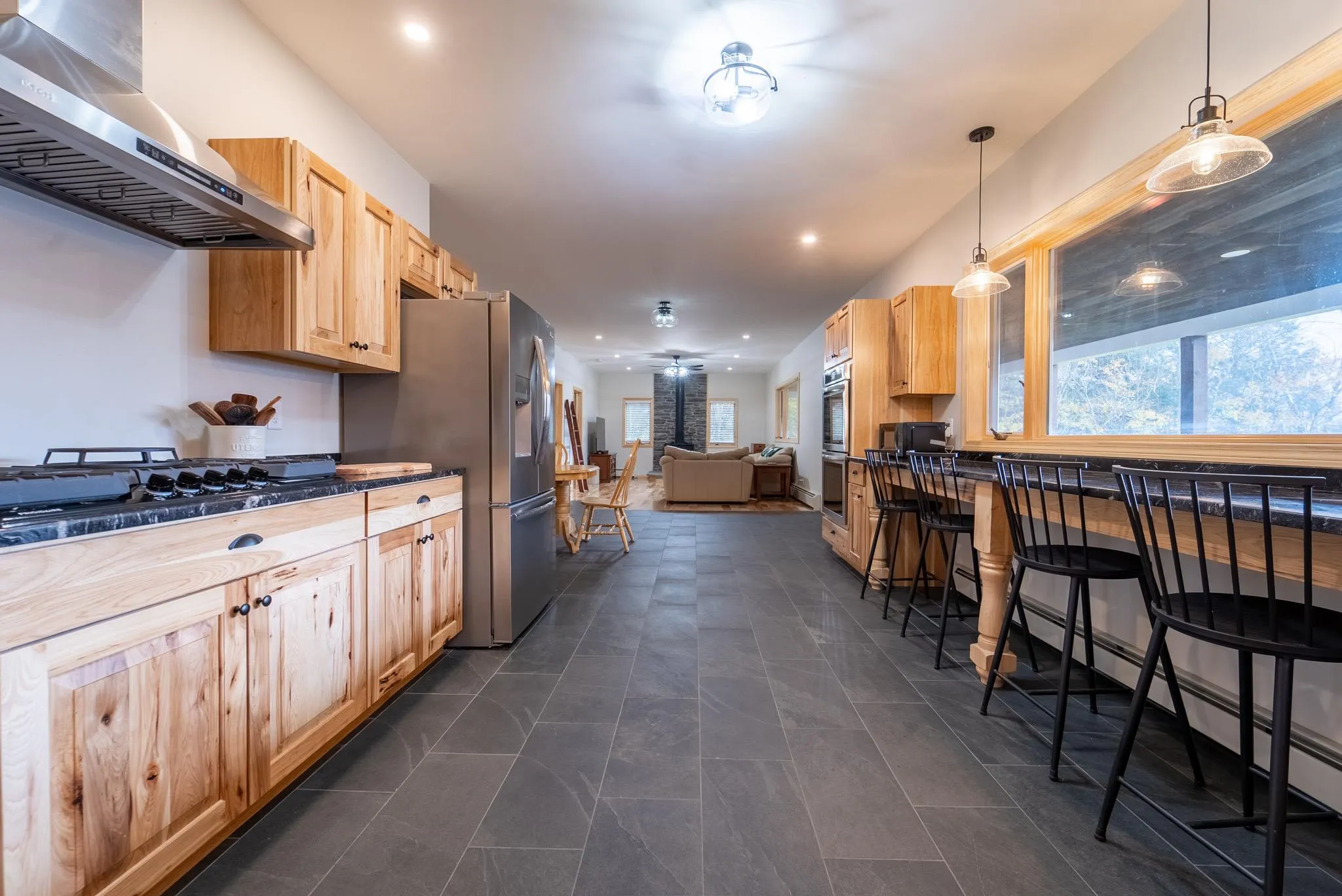 Kitchen featuring light brown cabinets, stainless steel appliances, hanging light fixtures, and range hood Kitchen featuring light brown cabinets, stainless steel appliances, hanging light fixtures, and range hood
