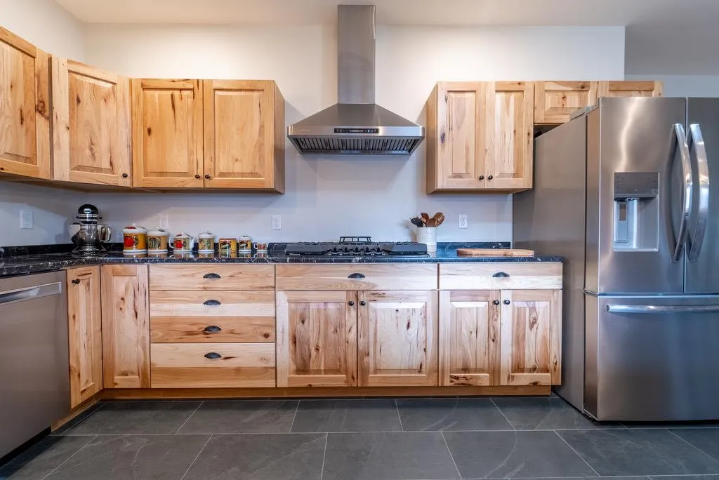 Kitchen featuring appliances with stainless steel finishes, light brown cabinetry, dark stone counters, and wall chimney range hood Kitchen featuring appliances with stainless steel finishes, light brown cabinetry, dark stone counters, and wall chimney range hood