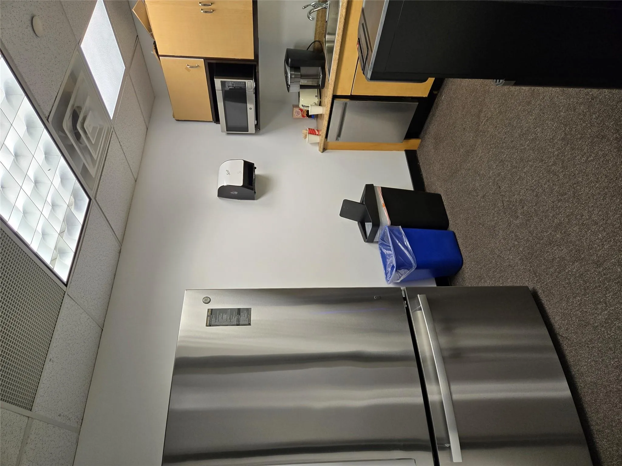 Kitchen featuring refrigerator, dishwasher, carpet flooring, a drop ceiling, and light countertops Kitchen featuring refrigerator, dishwasher, carpet flooring, a drop ceiling, and light countertops