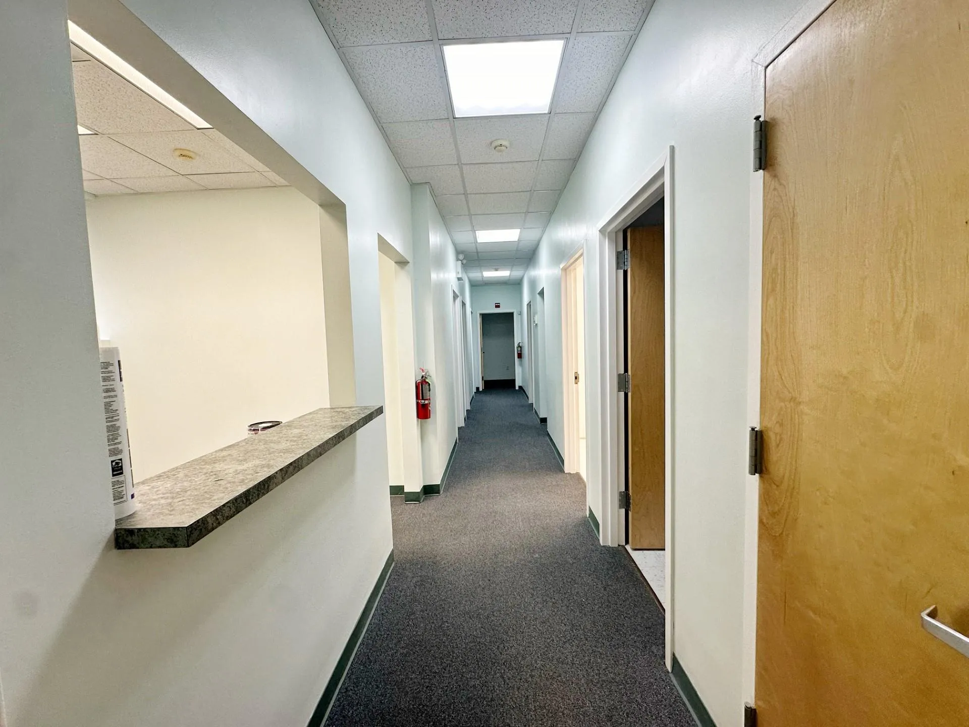 Hall with a drop ceiling and dark colored carpet Hall with a drop ceiling and dark colored carpet