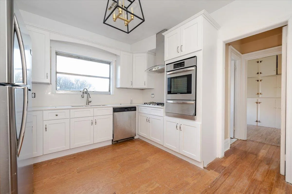Kitchen with stainless steel appliances, pendant lighting, sink, white cabinetry, and wall chimney range hood Kitchen with stainless steel appliances, pendant lighting, sink, white cabinetry, and wall chimney range hood