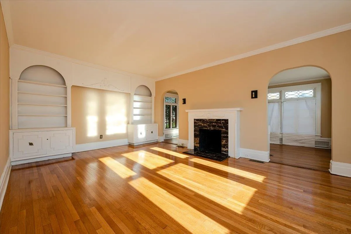 Unfurnished living room with a high end fireplace, built in features, ornamental molding, and wood-type flooring Unfurnished living room with a high end fireplace, built in features, ornamental molding, and wood-type flooring