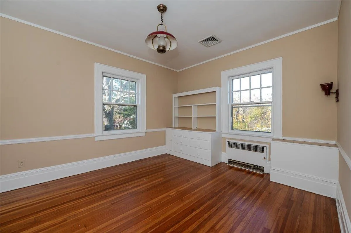 Unfurnished room featuring radiator, plenty of natural light, crown molding, and dark hardwood / wood-style floors Unfurnished room featuring radiator, plenty of natural light, crown molding, and dark hardwood / wood-style floors