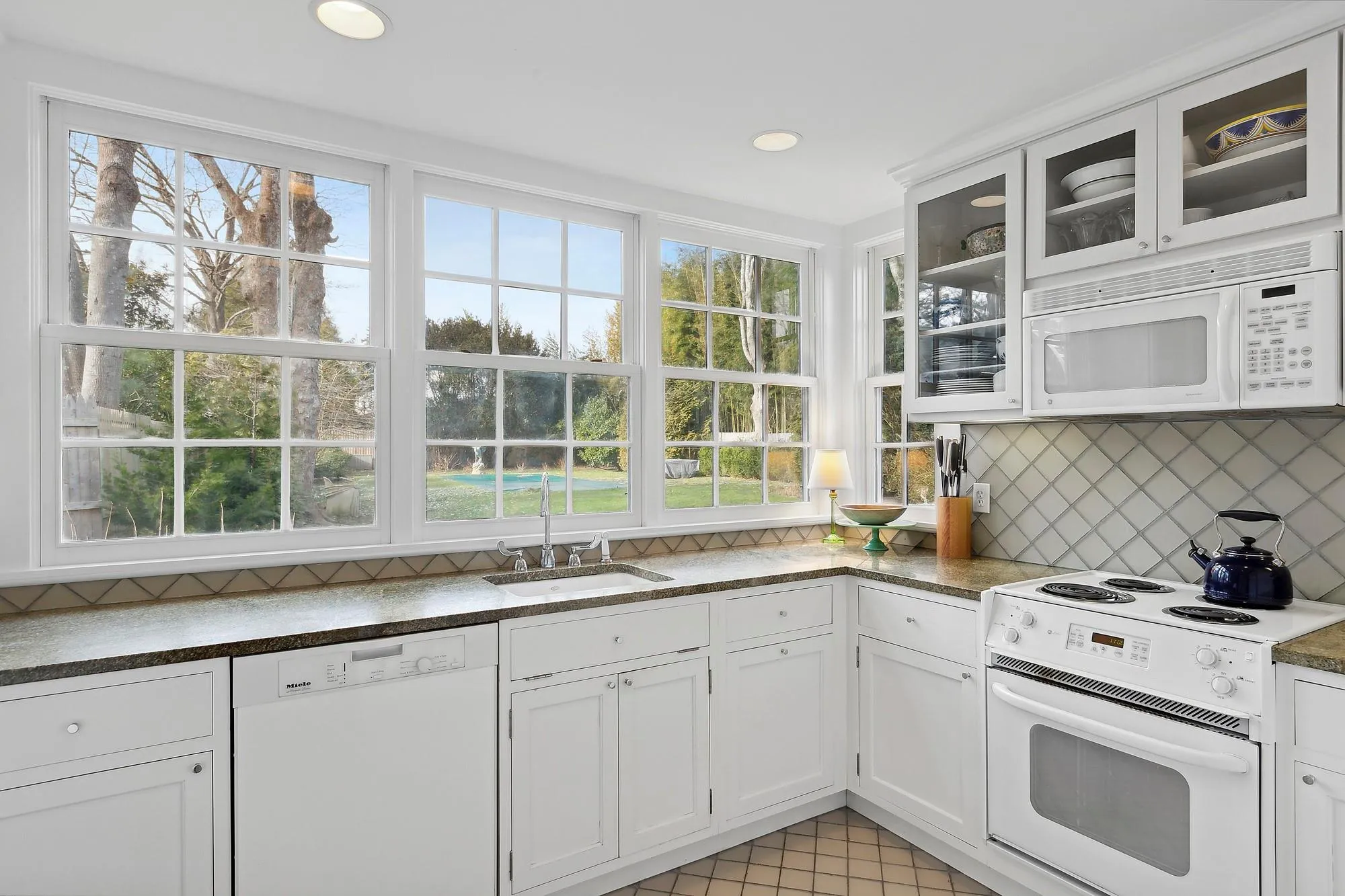 Kitchen featuring white appliances, white cabinets, sink, tasteful backsplash, and light tile patterned flooring Kitchen featuring white appliances, white cabinets, sink, tasteful backsplash, and light tile patterned flooring
