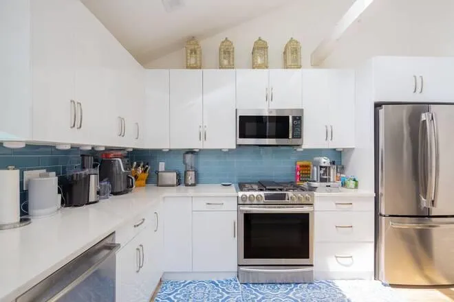 Kitchen featuring vaulted ceiling, appliances with stainless steel finishes, white cabinets, and tasteful backsplash Kitchen featuring vaulted ceiling, appliances with stainless steel finishes, white cabinets, and tasteful backsplash
