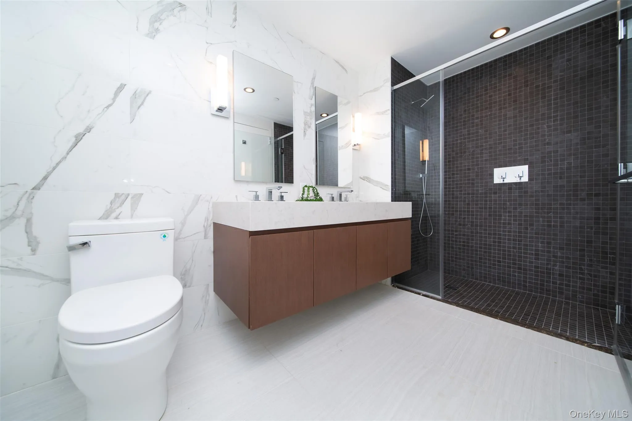 Bathroom featuring toilet, a shower with shower door, tile walls, and vanity Bathroom featuring toilet, a shower with shower door, tile walls, and vanity