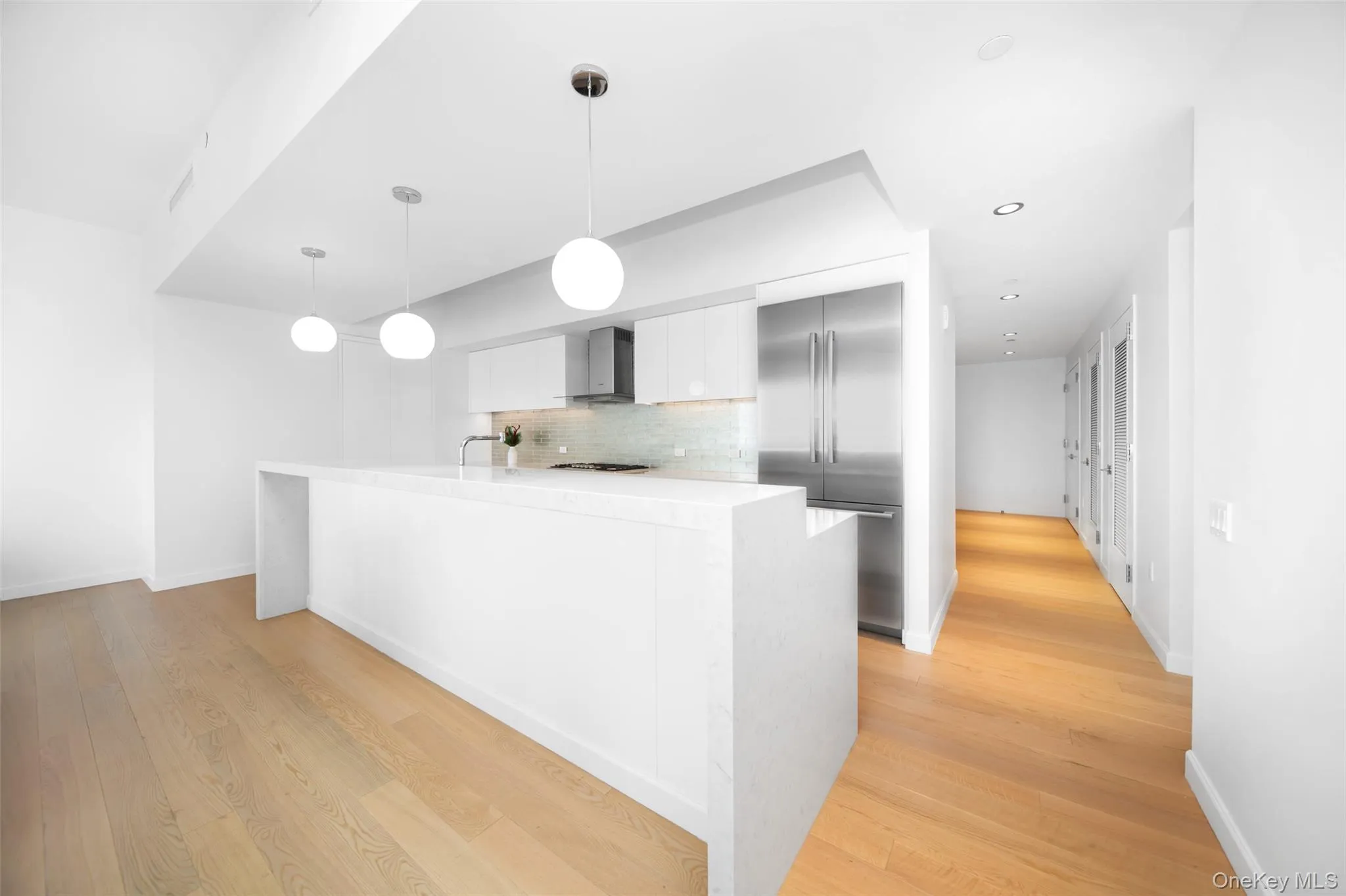 Kitchen with stainless steel built in refrigerator, light hardwood / wood-style floors, pendant lighting, and wall chimney exhaust hood Kitchen with stainless steel built in refrigerator, light hardwood / wood-style floors, pendant lighting, and wall chimney exhaust hood