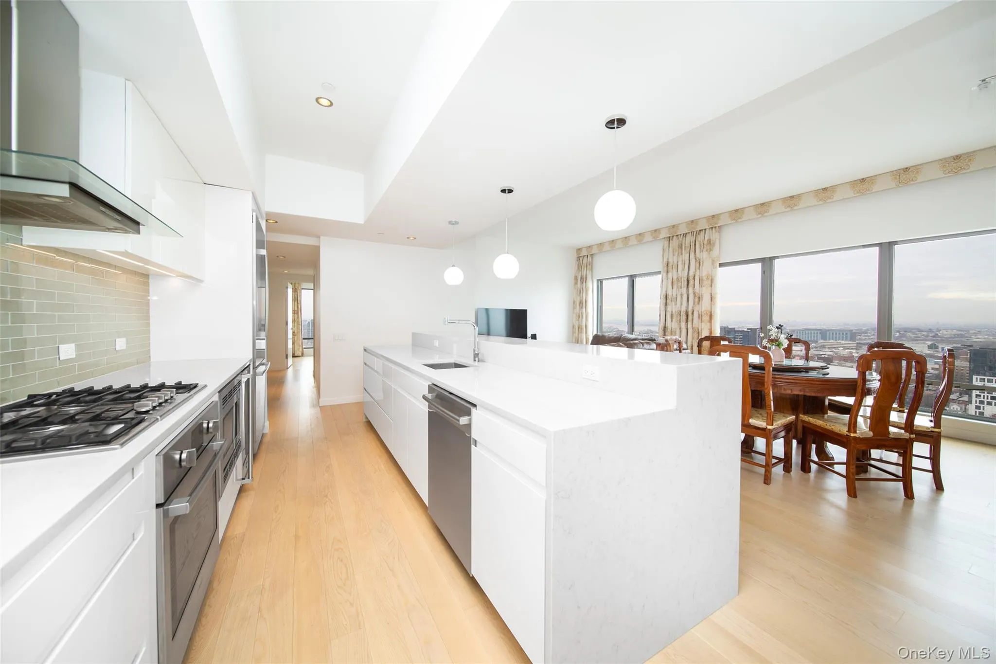 Kitchen with decorative light fixtures, stainless steel appliances, wall chimney range hood, and white cabinetry Kitchen with decorative light fixtures, stainless steel appliances, wall chimney range hood, and white cabinetry