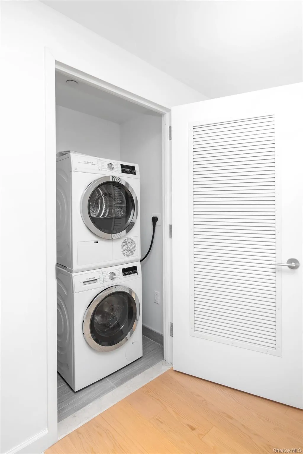 Laundry area with stacked washer and clothes dryer and hardwood / wood-style floors Laundry area with stacked washer and clothes dryer and hardwood / wood-style floors