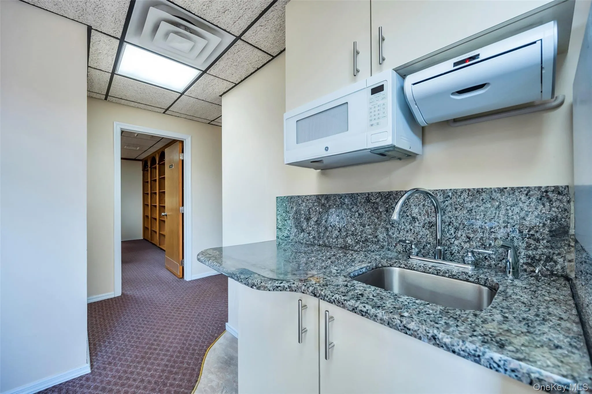 Kitchen featuring sink, white cabinetry, a paneled ceiling, dark carpet, and stone countertops Kitchen featuring sink, white cabinetry, a paneled ceiling, dark carpet, and stone countertops