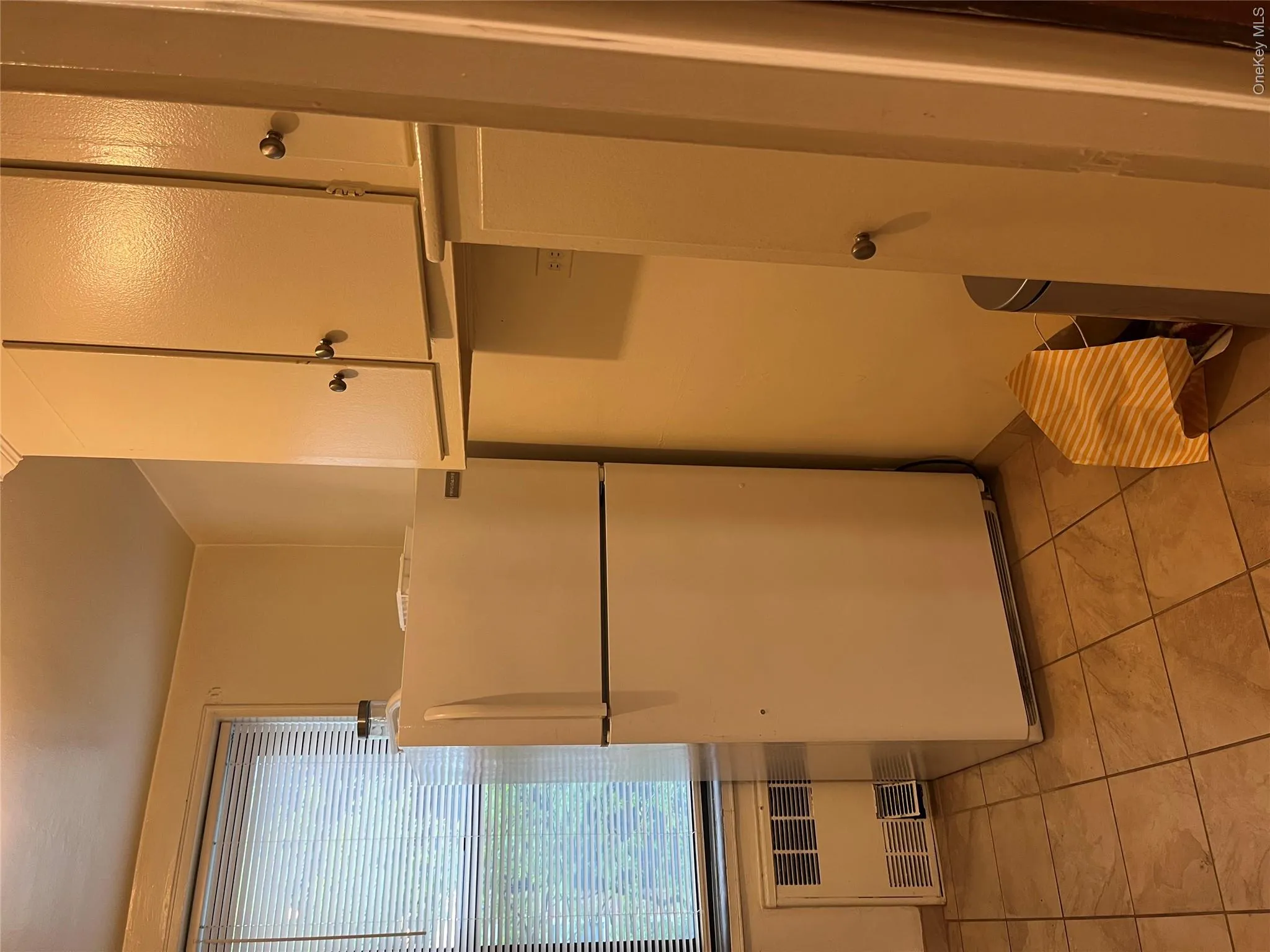 Kitchen with light tile patterned floors, white refrigerator, white cabinets, and radiator heating unit Kitchen with light tile patterned floors, white refrigerator, white cabinets, and radiator heating unit