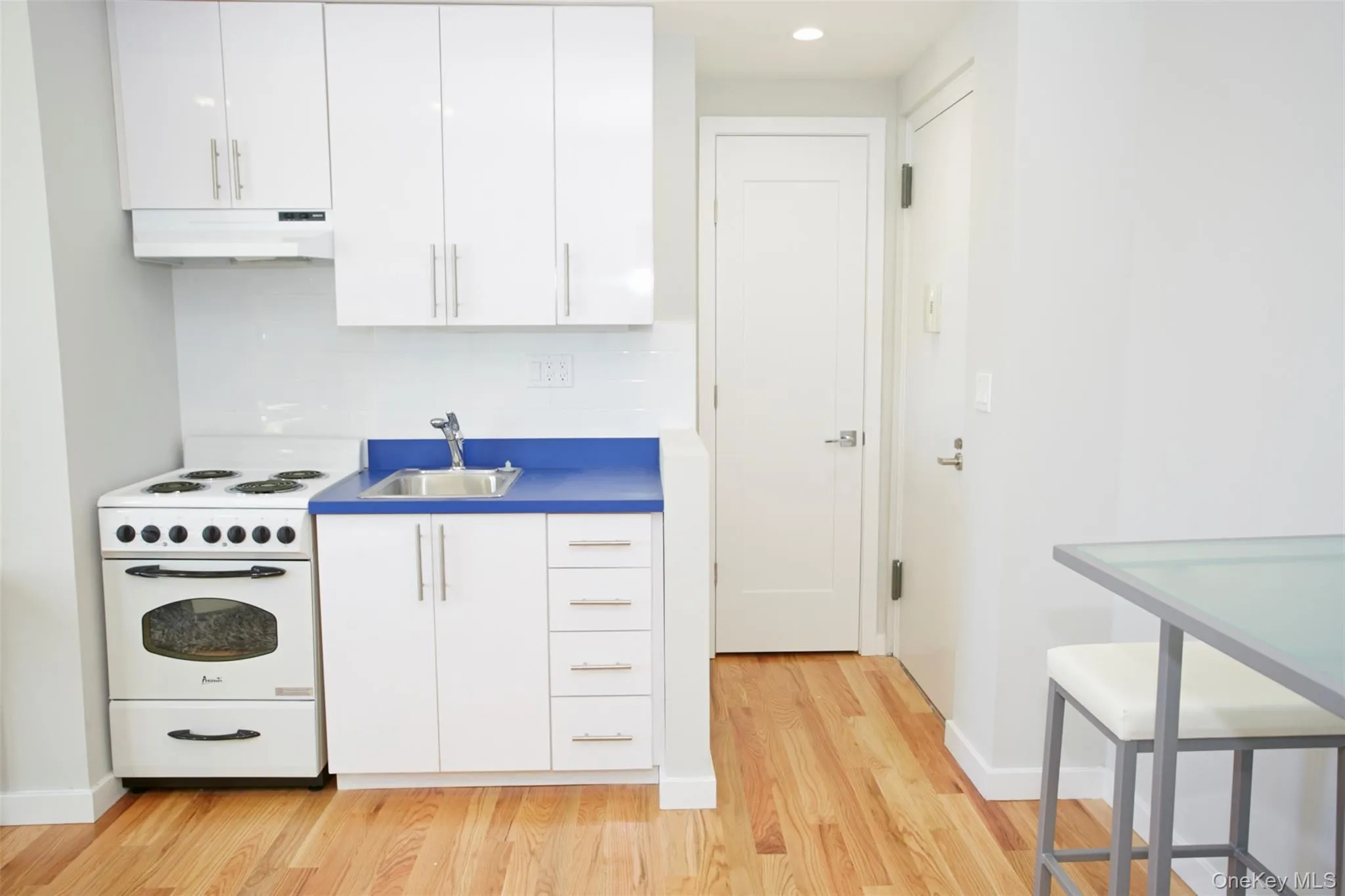 Kitchen with electric stove, white cabinets, light wood finished floors, under cabinet range hood, and tasteful backsplash Kitchen with electric stove, white cabinets, light wood finished floors, under cabinet range hood, and tasteful backsplash