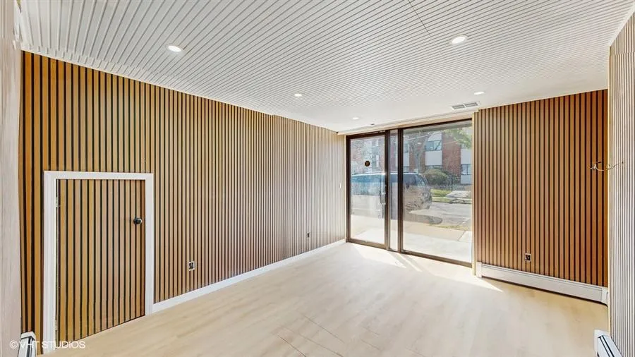 Unfurnished room with visible vents, wooden walls, wood finished floors, baseboard heating, and expansive windows Unfurnished room with visible vents, wooden walls, wood finished floors, baseboard heating, and expansive windows