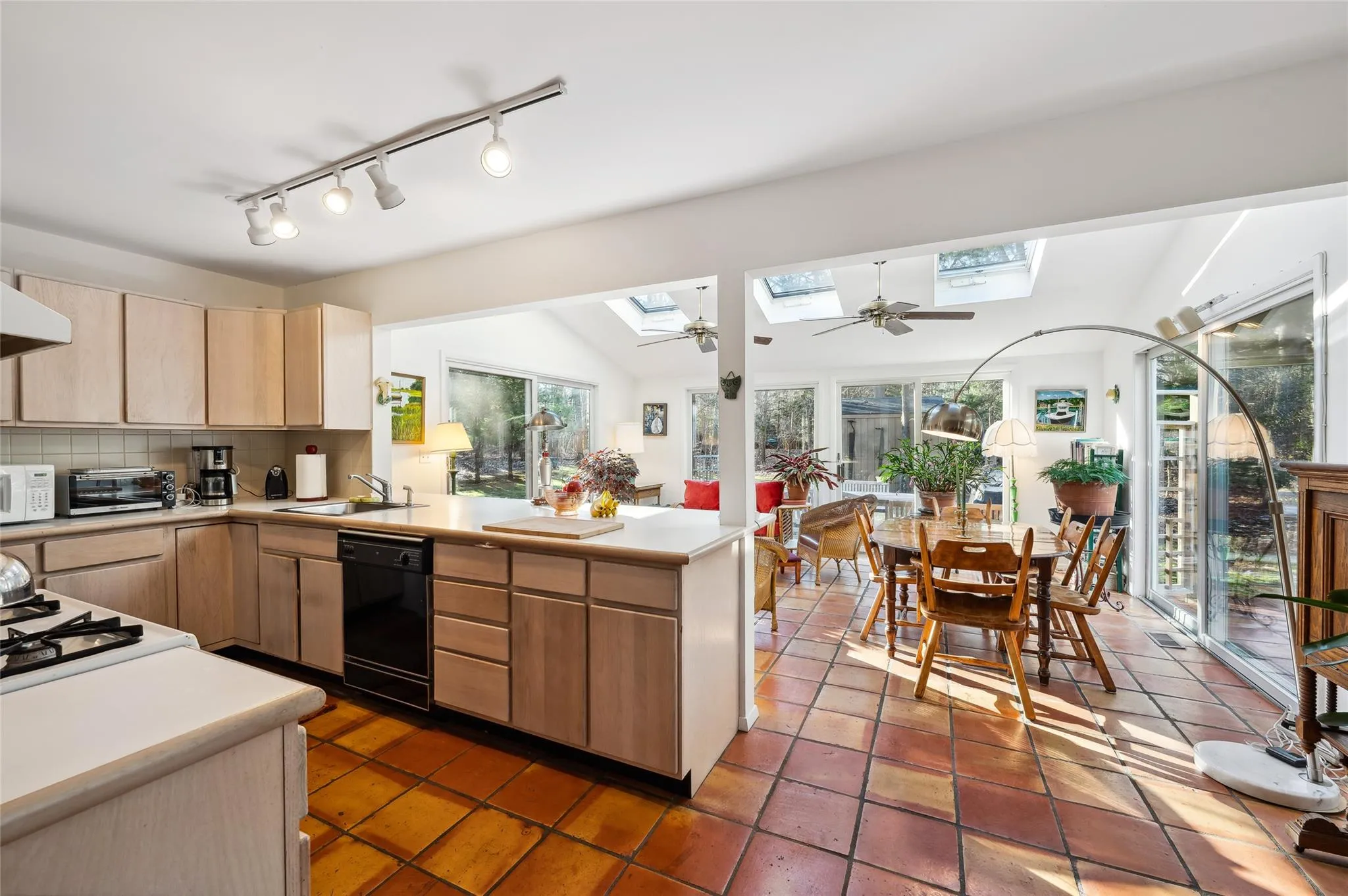 Kitchen featuring black dishwasher, backsplash, light brown cabinets, vaulted ceiling with skylight, and sink Kitchen featuring black dishwasher, backsplash, light brown cabinets, vaulted ceiling with skylight, and sink