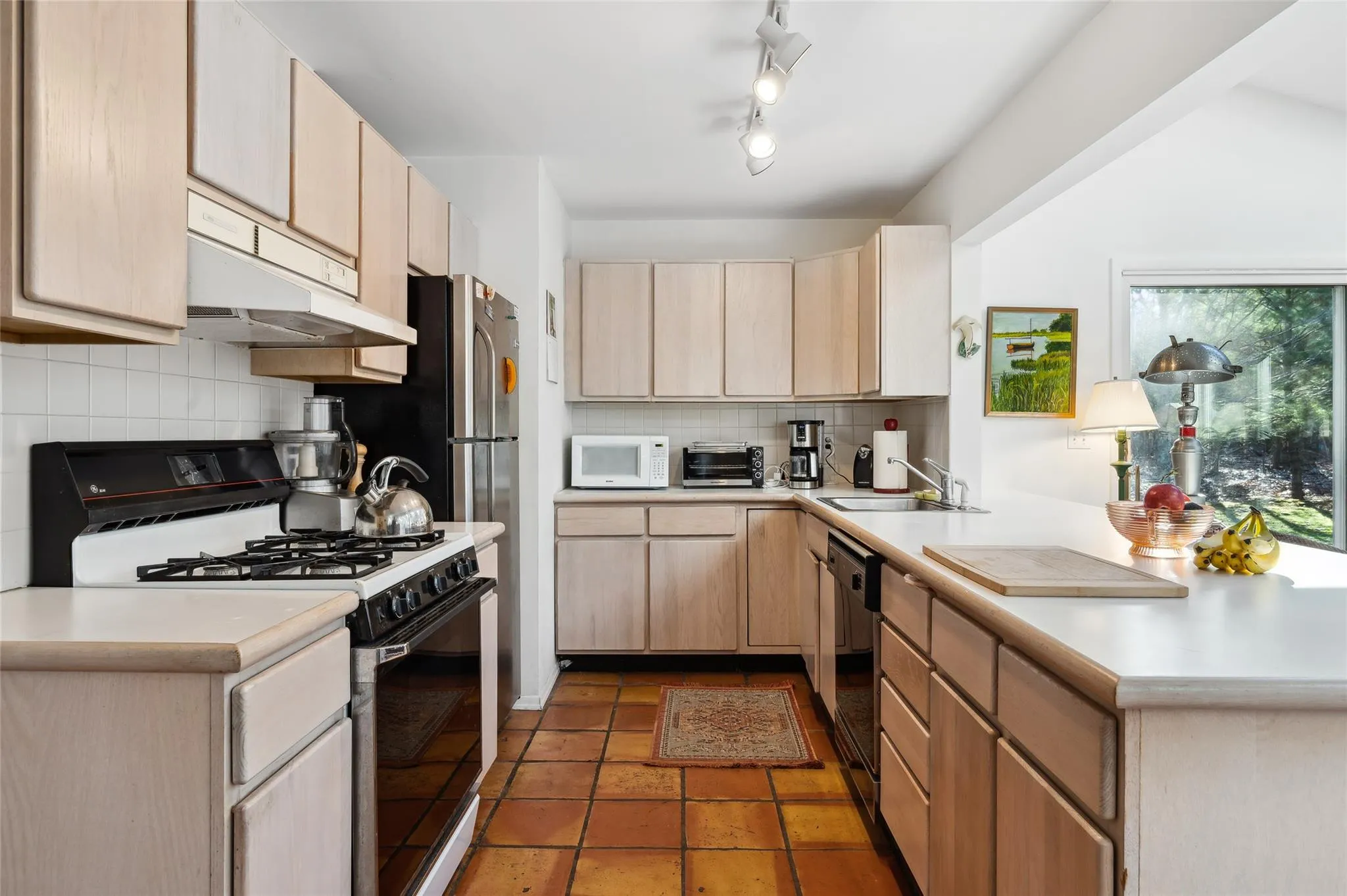 Kitchen with light brown cabinetry, decorative backsplash, gas range, and sink Kitchen with light brown cabinetry, decorative backsplash, gas range, and sink