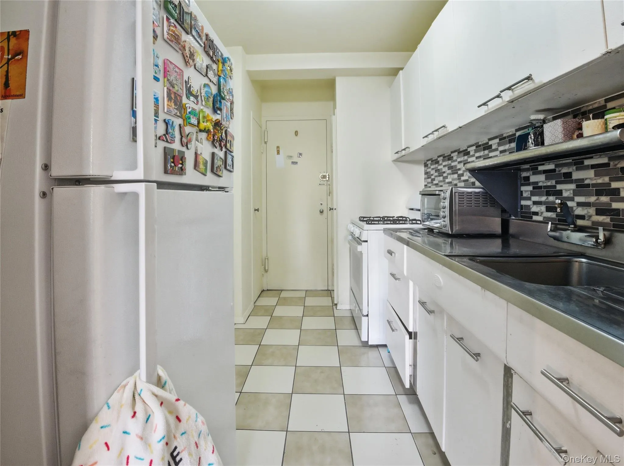 Kitchen with white cabinets, white appliances, dark countertops, and tasteful backsplash Kitchen with white cabinets, white appliances, dark countertops, and tasteful backsplash