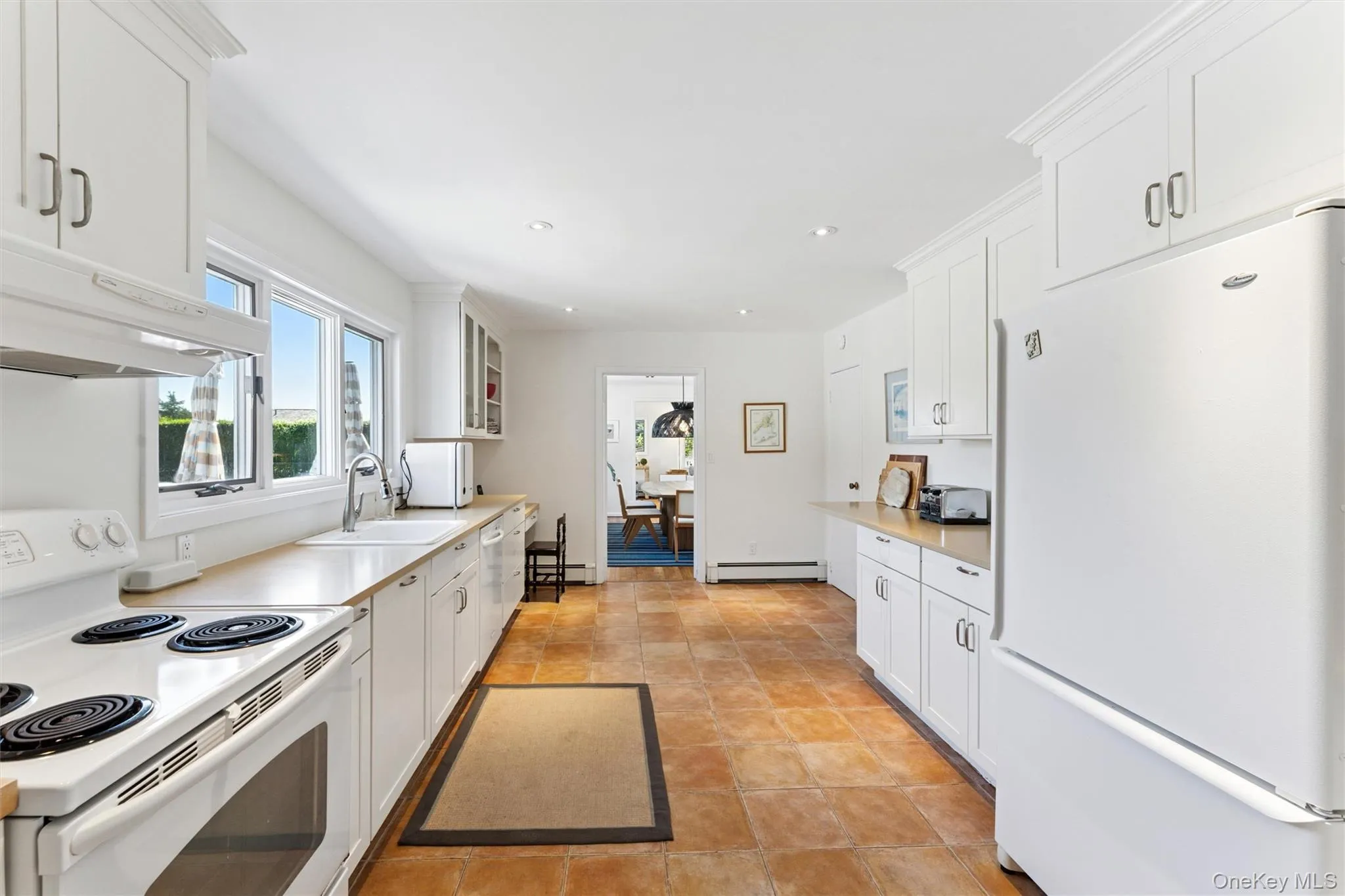 Kitchen featuring white appliances, white cabinetry, light countertops, glass insert cabinets, and recessed lighting Kitchen featuring white appliances, white cabinetry, light countertops, glass insert cabinets, and recessed lighting