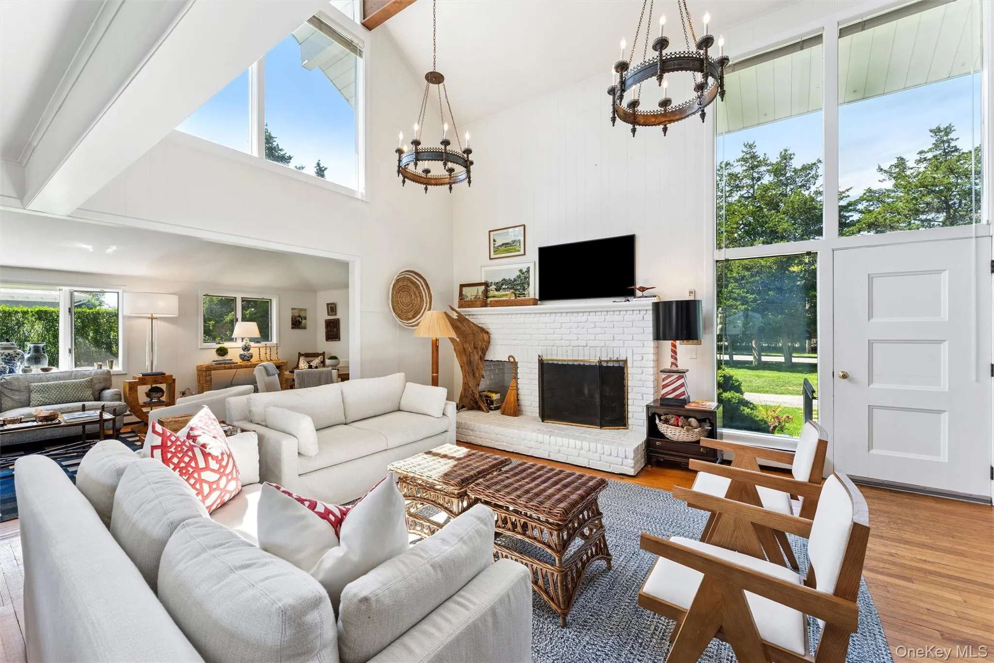 Living room featuring wood finished floors, a towering ceiling, a brick fireplace, and a chandelier Living room featuring wood finished floors, a towering ceiling, a brick fireplace, and a chandelier