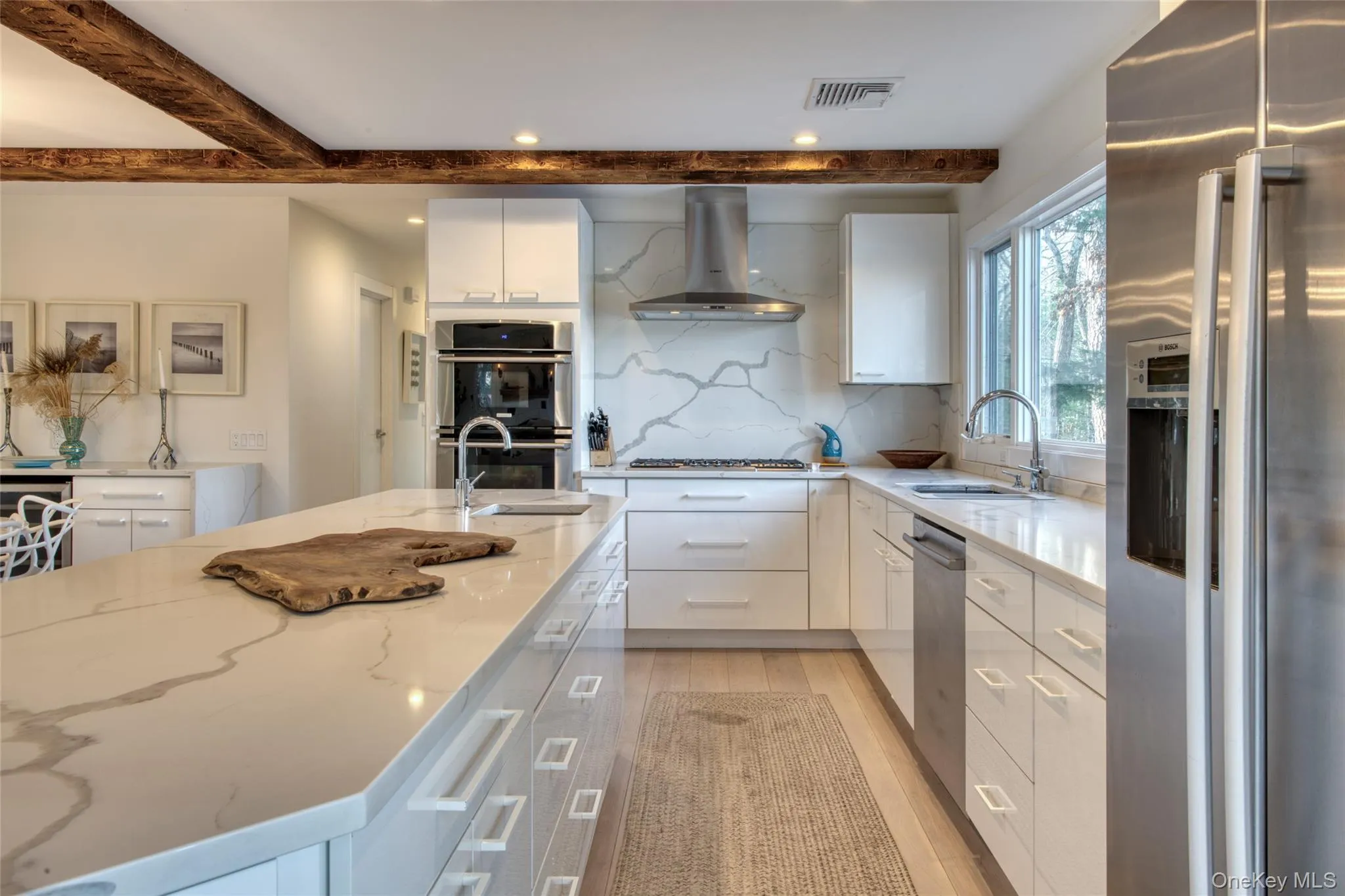 Kitchen featuring wall chimney exhaust hood, a sink, beam ceiling, stainless steel appliances, and backsplash Kitchen featuring wall chimney exhaust hood, a sink, beam ceiling, stainless steel appliances, and backsplash