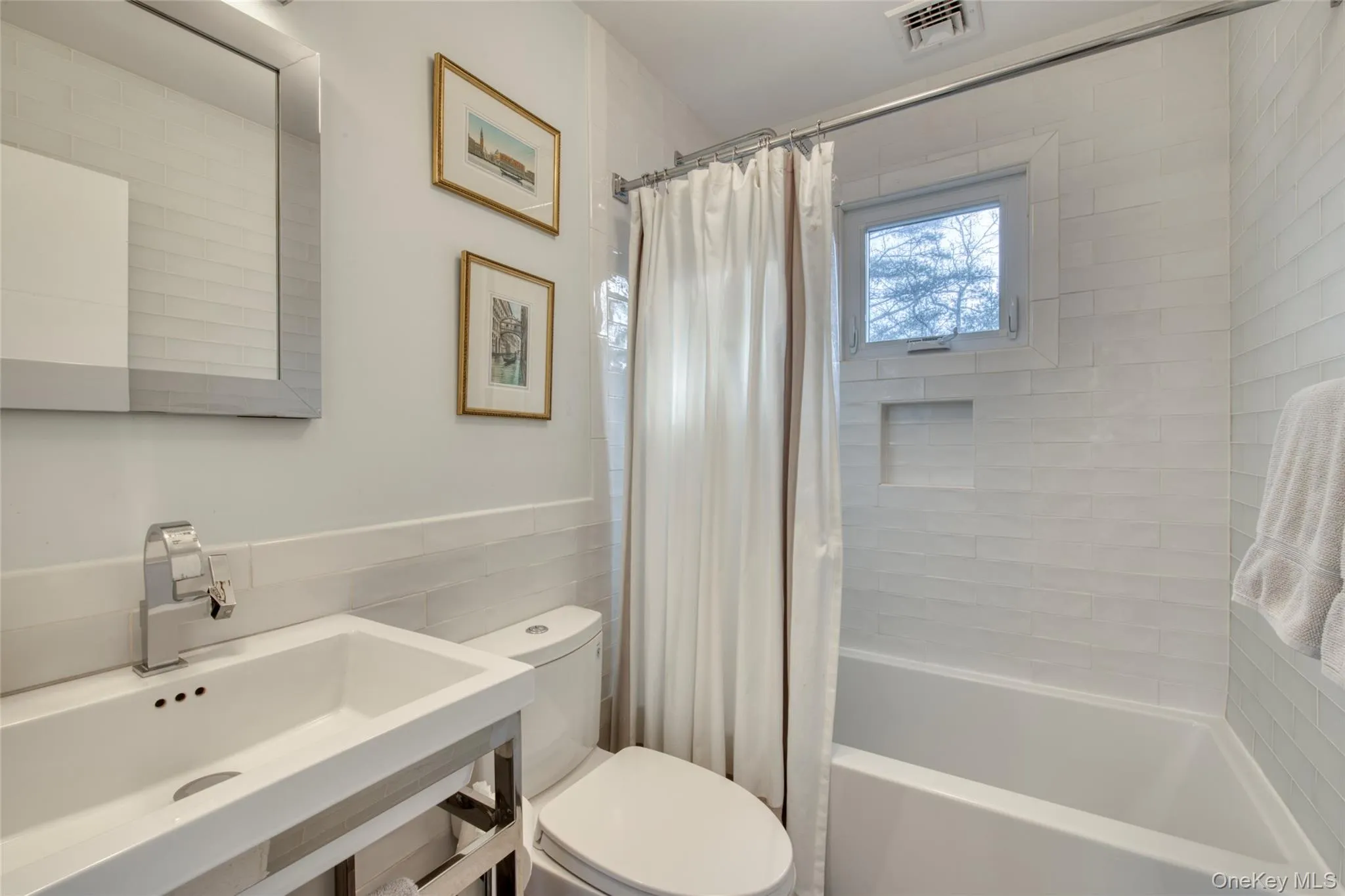 Bathroom with visible vents, toilet, a wainscoted wall, shower / bath combo with shower curtain, and a sink Bathroom with visible vents, toilet, a wainscoted wall, shower / bath combo with shower curtain, and a sink