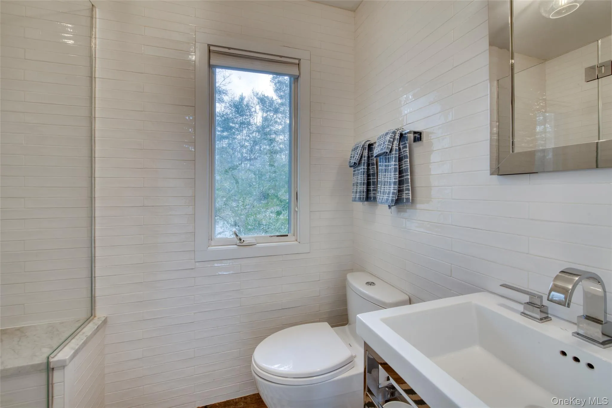 Bathroom featuring tiled shower, a sink, tile walls, and toilet Bathroom featuring tiled shower, a sink, tile walls, and toilet