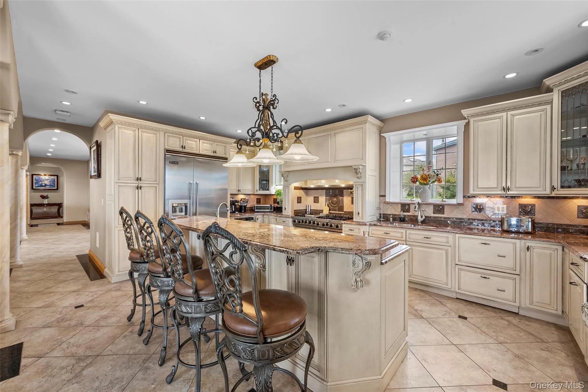 Kitchen with stainless steel built in refrigerator, dark stone countertops, cream cabinets, arched walkways, and range Kitchen with stainless steel built in refrigerator, dark stone countertops, cream cabinets, arched walkways, and range