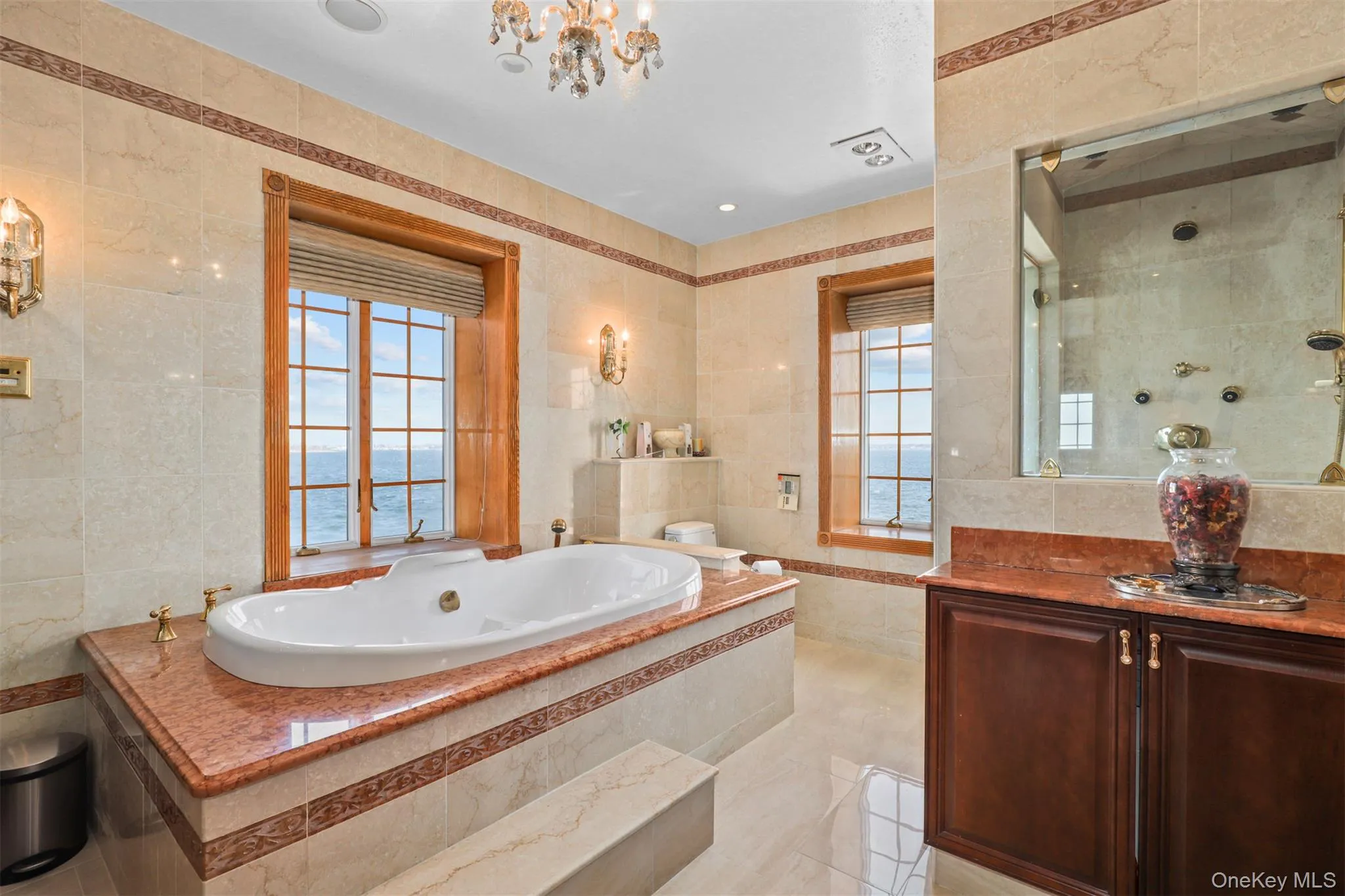 Bathroom with tile patterned flooring, a walk in shower, a jetted tub, a notable chandelier, and tile walls Bathroom with tile patterned flooring, a walk in shower, a jetted tub, a notable chandelier, and tile walls