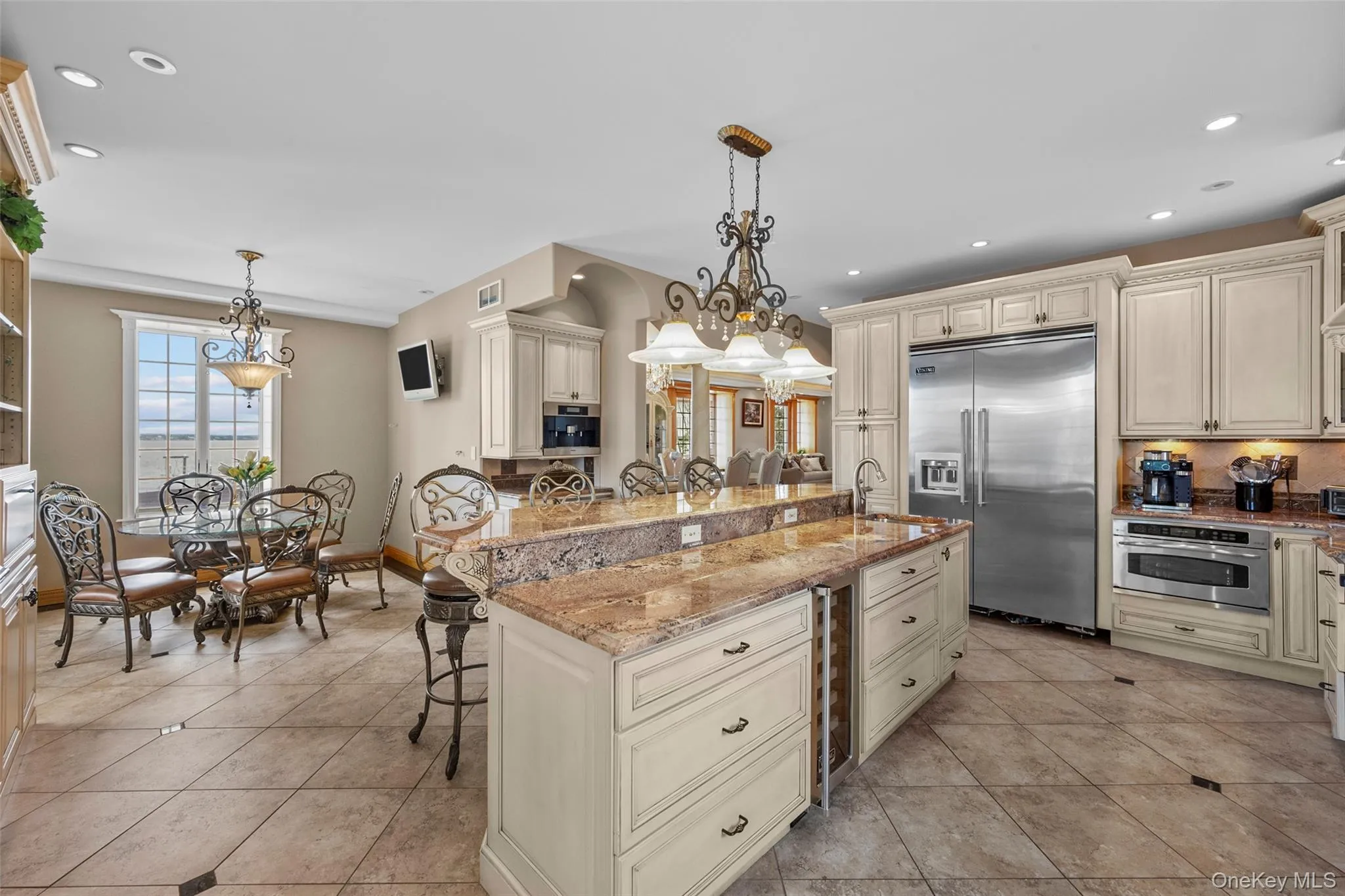 Kitchen with a breakfast bar area, light stone counters, recessed lighting, stainless steel appliances, and cream cabinetry Kitchen with a breakfast bar area, light stone counters, recessed lighting, stainless steel appliances, and cream cabinetry
