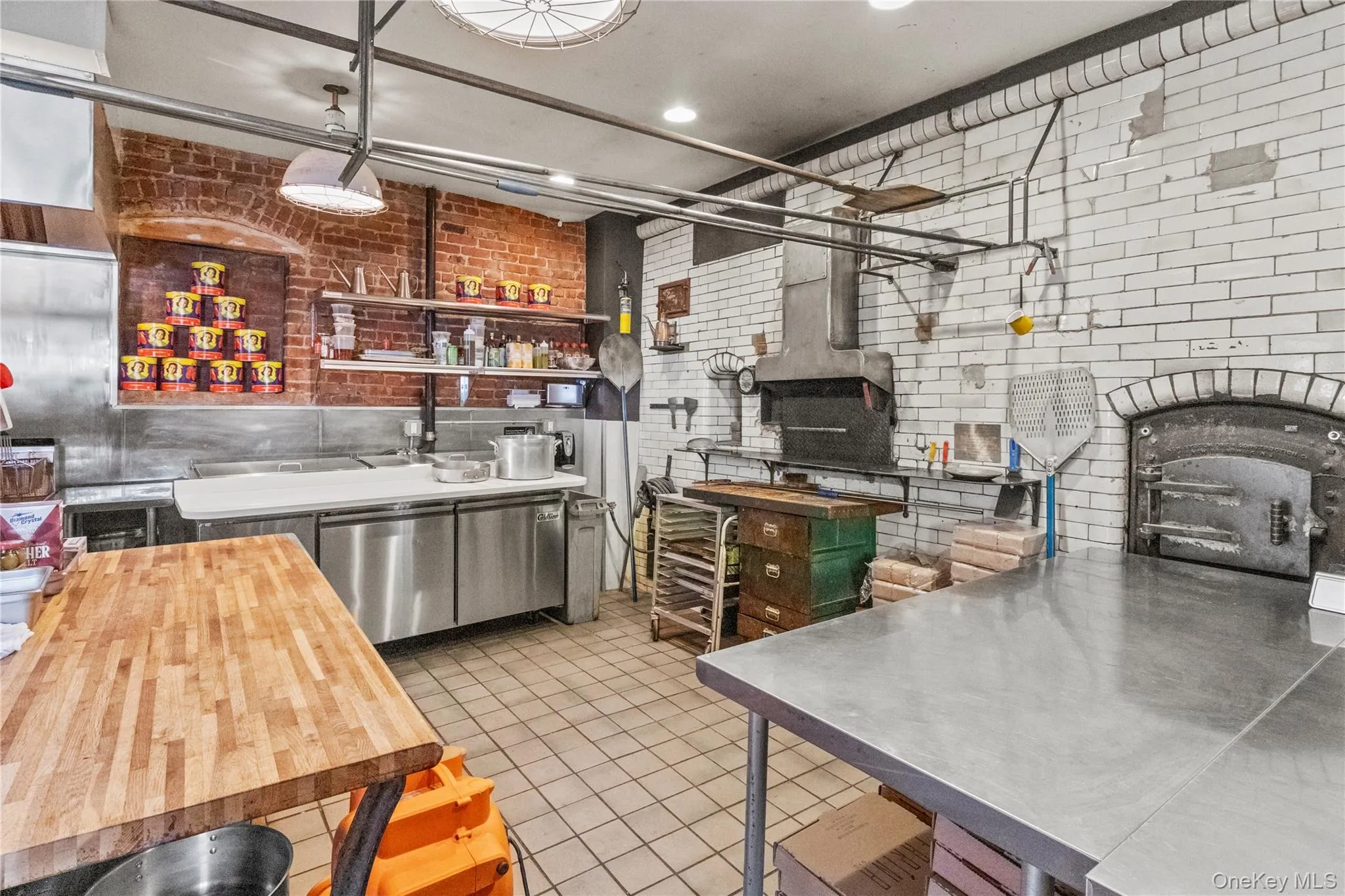 Kitchen featuring stainless steel counters, brick wall, dishwasher, and light tile patterned flooring Kitchen featuring stainless steel counters, brick wall, dishwasher, and light tile patterned flooring