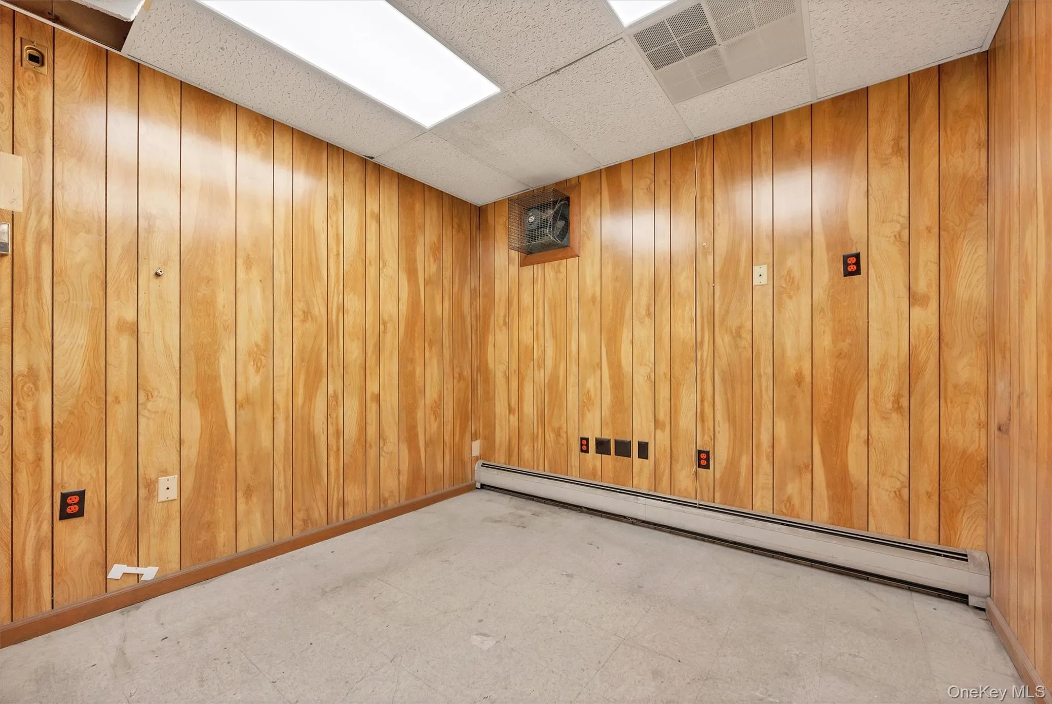 Empty room with a baseboard heating unit, a paneled ceiling, and wood walls Empty room with a baseboard heating unit, a paneled ceiling, and wood walls