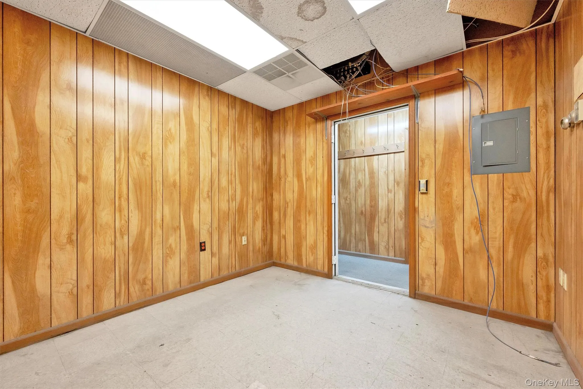Unfurnished room with a paneled ceiling, electric panel, and wood walls Unfurnished room with a paneled ceiling, electric panel, and wood walls