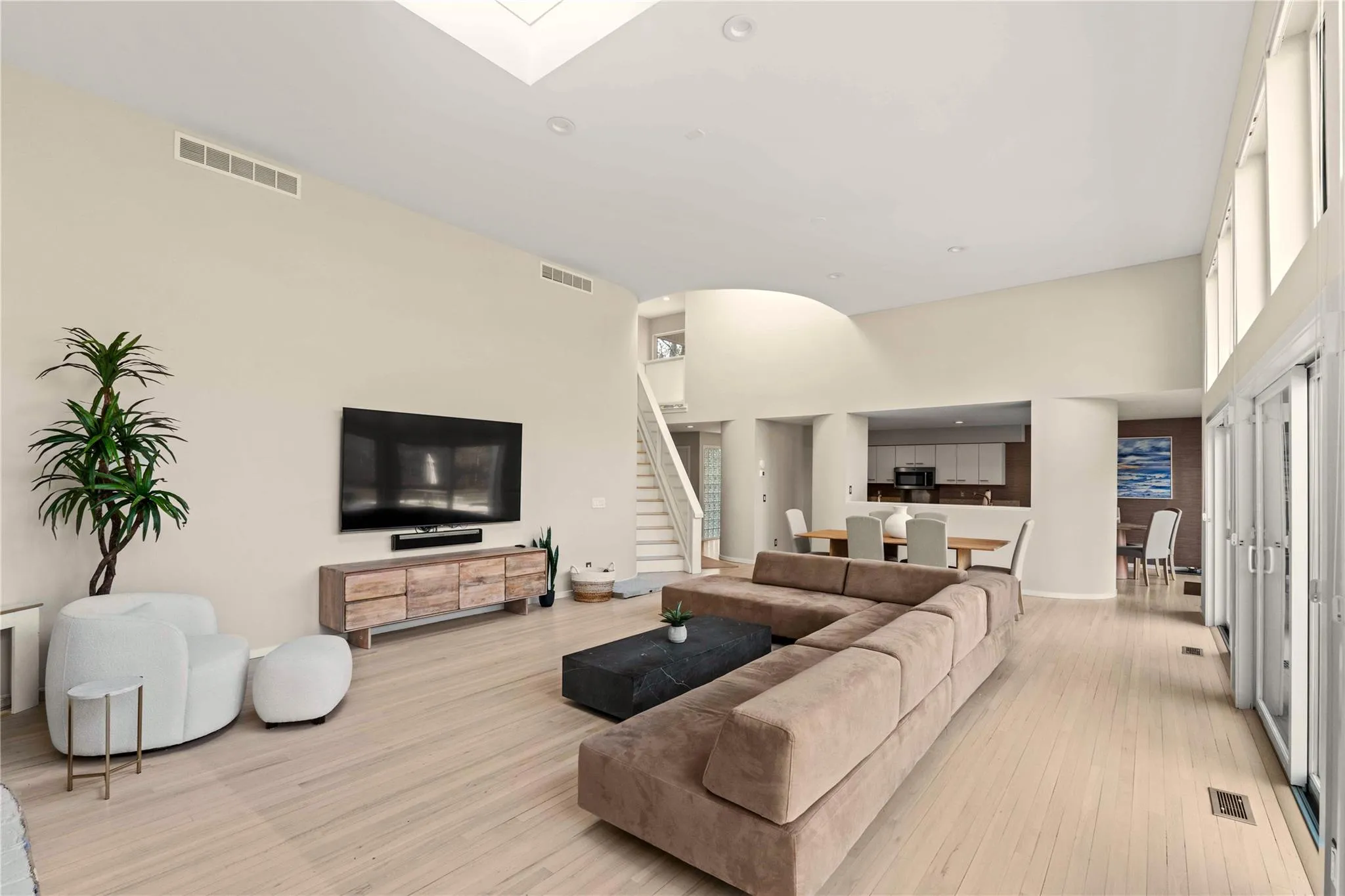 Living room featuring a skylight, light hardwood / wood-style floors, and a high ceiling Living room featuring a skylight, light hardwood / wood-style floors, and a high ceiling