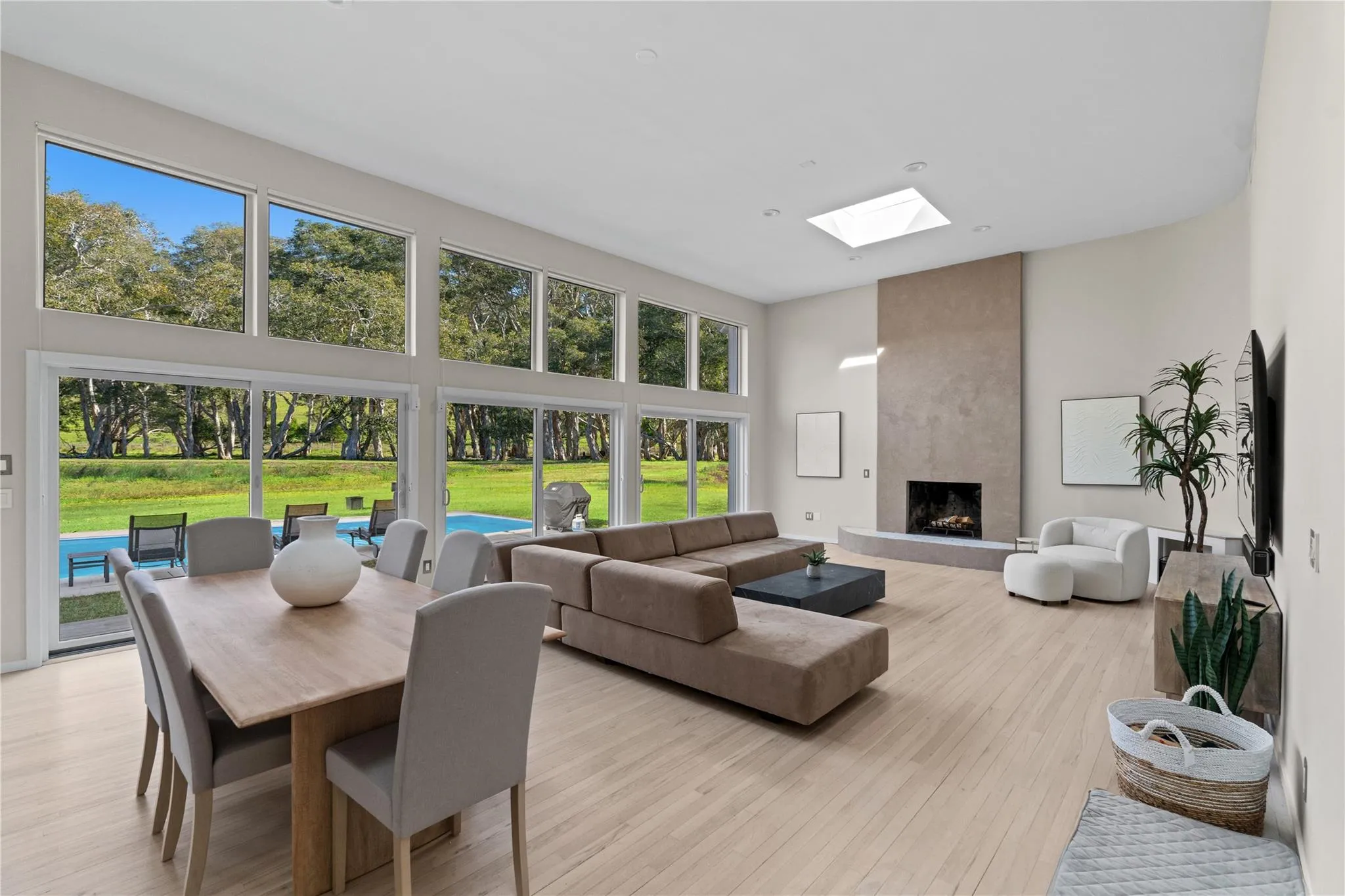 Living area featuring a towering ceiling, a large fireplace, light wood-style flooring, and a skylight Living area featuring a towering ceiling, a large fireplace, light wood-style flooring, and a skylight