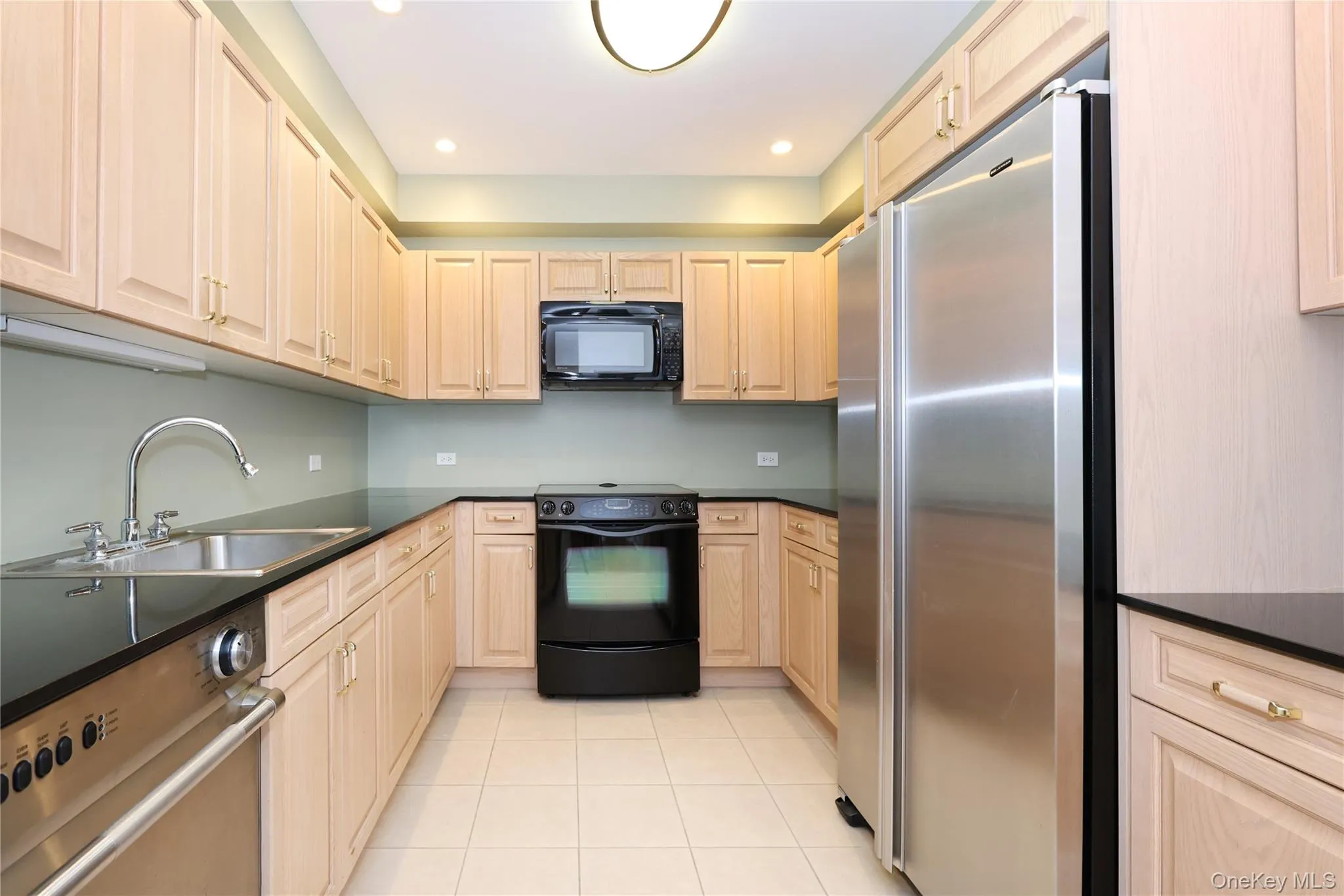 Kitchen with black appliances, light tile patterned floors, recessed lighting, light brown cabinets, and dark stone countertops Kitchen with black appliances, light tile patterned floors, recessed lighting, light brown cabinets, and dark stone countertops