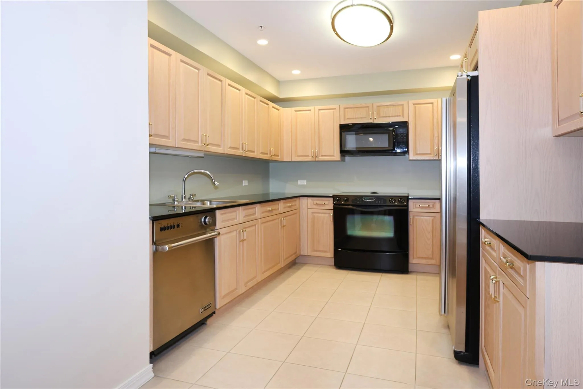 Kitchen with black appliances, light brown cabinetry, light tile patterned floors, recessed lighting, and dark stone counters Kitchen with black appliances, light brown cabinetry, light tile patterned floors, recessed lighting, and dark stone counters