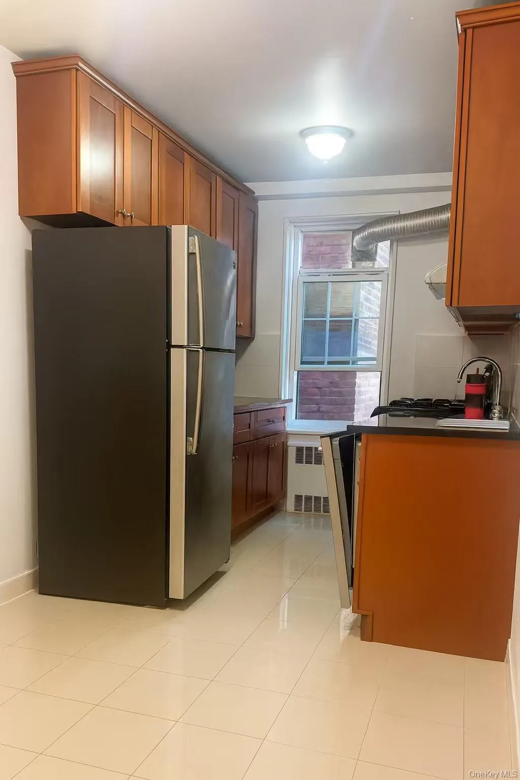 Kitchen with freestanding refrigerator, light tile patterned floors, radiator, and brown cabinets Kitchen with freestanding refrigerator, light tile patterned floors, radiator, and brown cabinets