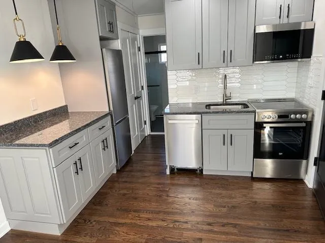 Kitchen featuring pendant lighting, sink, dark stone countertops, dark hardwood / wood-style flooring, and stainless steel appliances Kitchen featuring pendant lighting, sink, dark stone countertops, dark hardwood / wood-style flooring, and stainless steel appliances