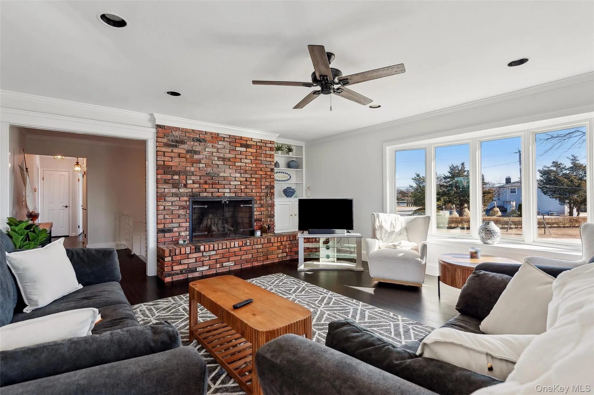 Living room featuring ornamental molding, a brick fireplace, wood-type flooring, and built in features Living room featuring ornamental molding, a brick fireplace, wood-type flooring, and built in features