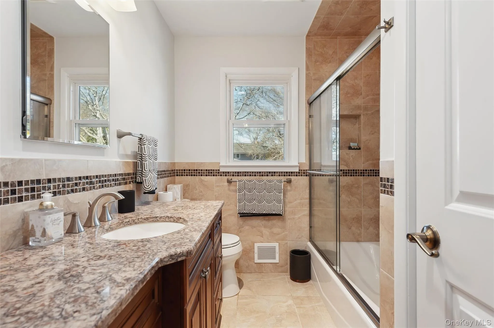 Full bathroom with vanity, tile walls, shower / bath combination with glass door, and toilet Full bathroom with vanity, tile walls, shower / bath combination with glass door, and toilet